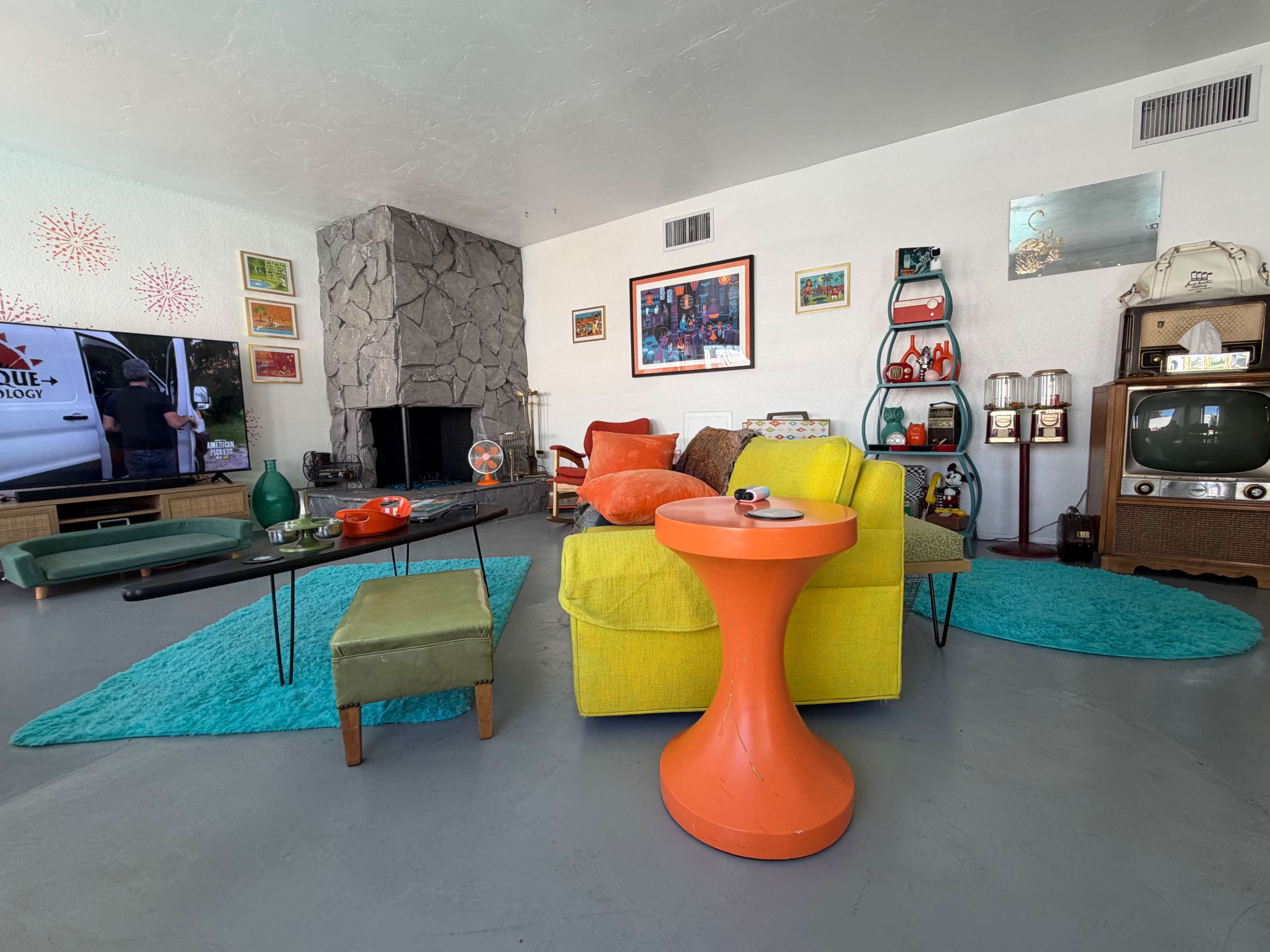 The living room features a vibrant, retro-inspired decor with a yellow sofa, an orange side table, and a green rug, along with various colorful furnishings and decorations.