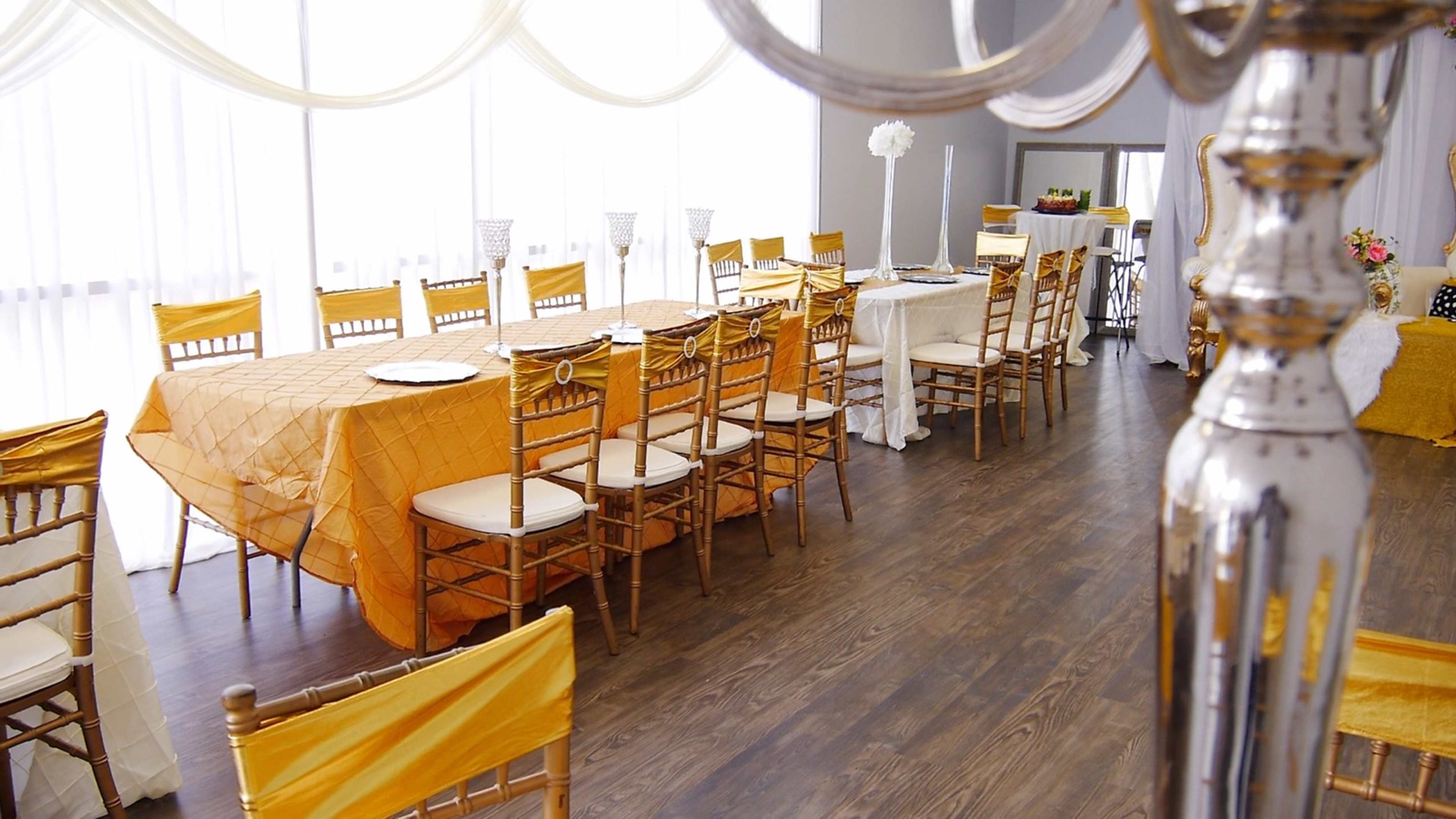 An elegantly arranged dining area with gold-colored tablecloths and wooden chairs, bathed in natural light from large windows.