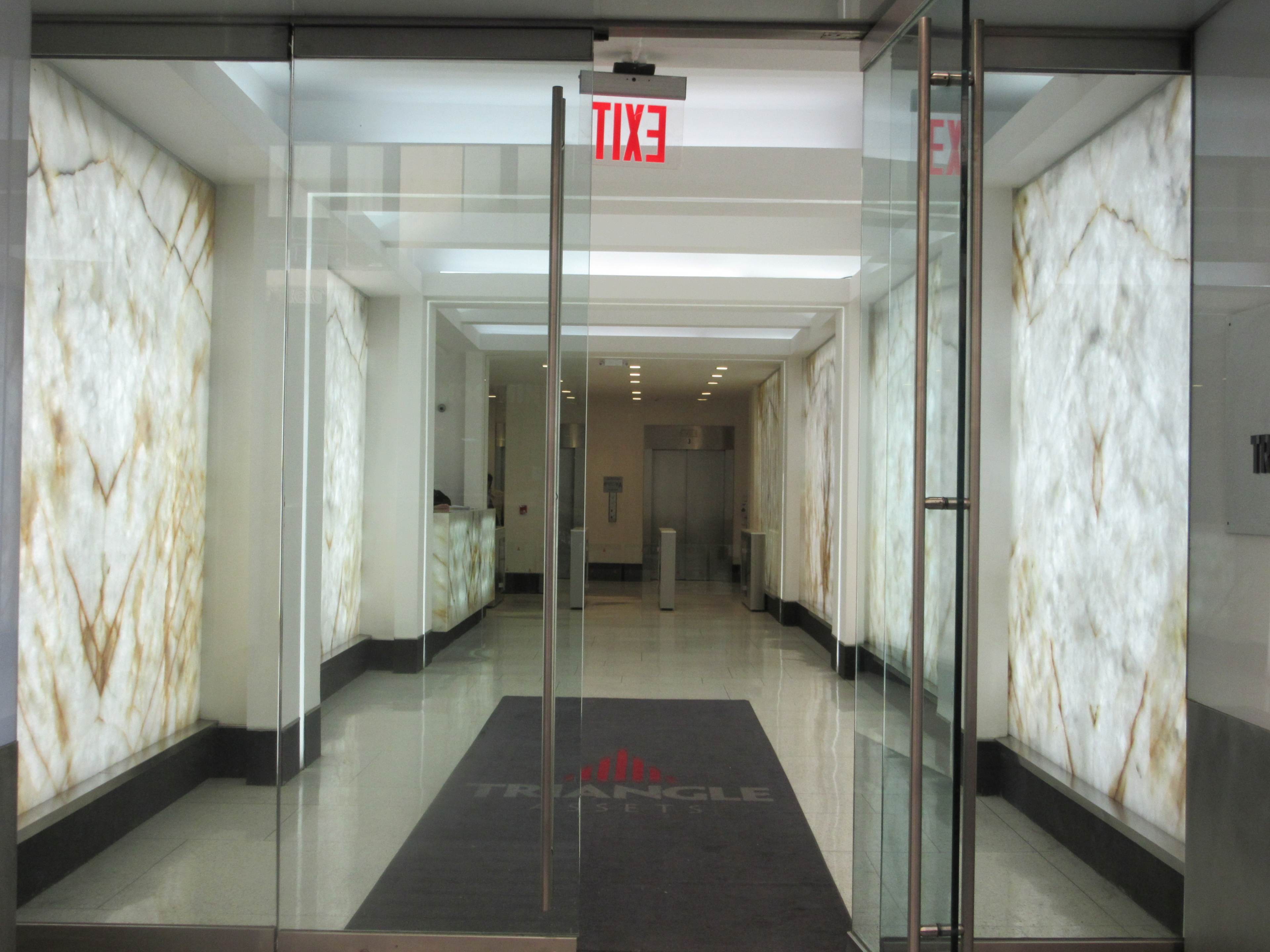 A modern entrance to a building with glass doors and decorative lit walls, featuring the word "EXIT" above.