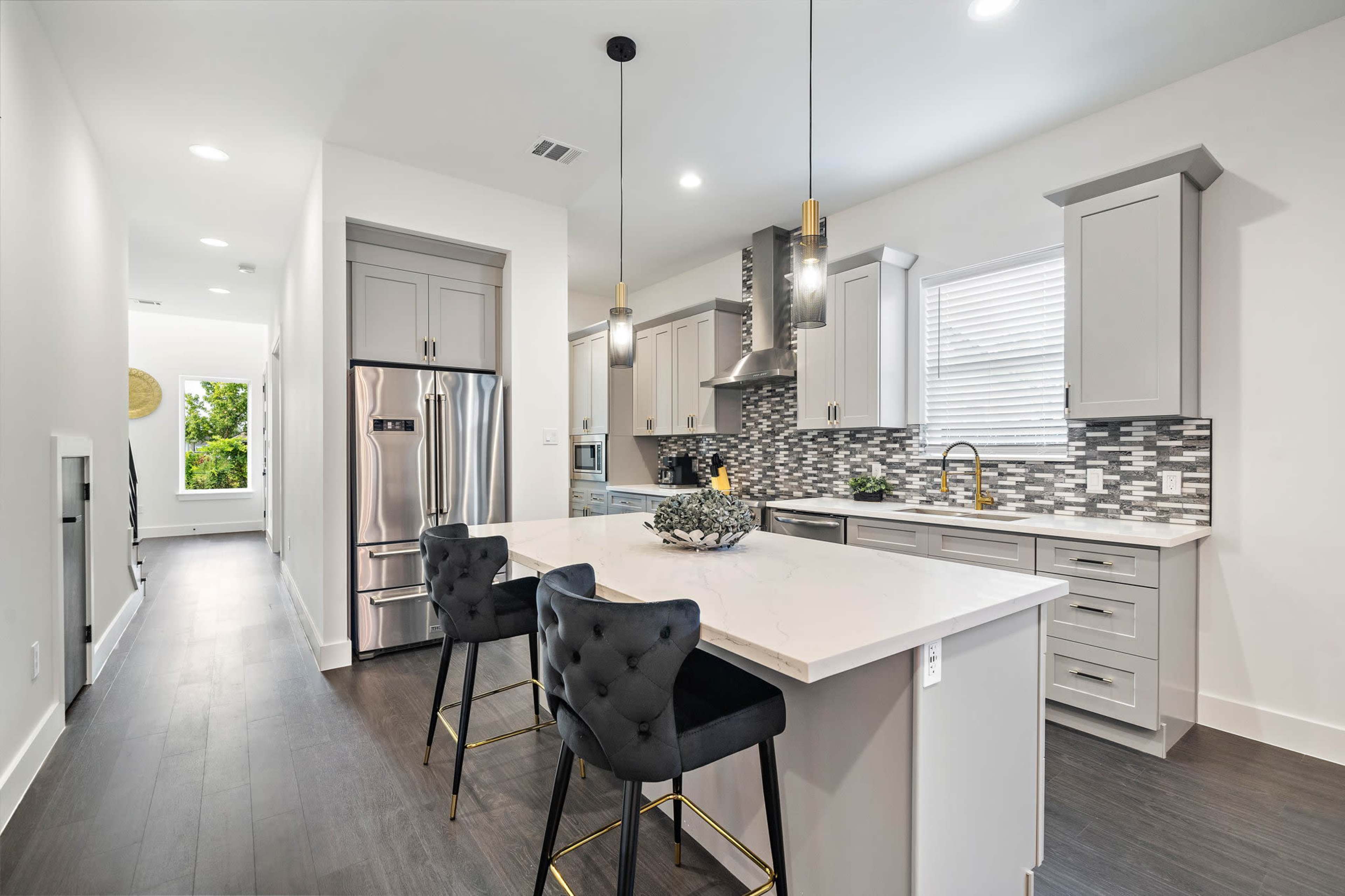 A modern kitchen features sleek cabinetry, stainless steel appliances, and a large island with bar seating, illuminated by pendant lights.