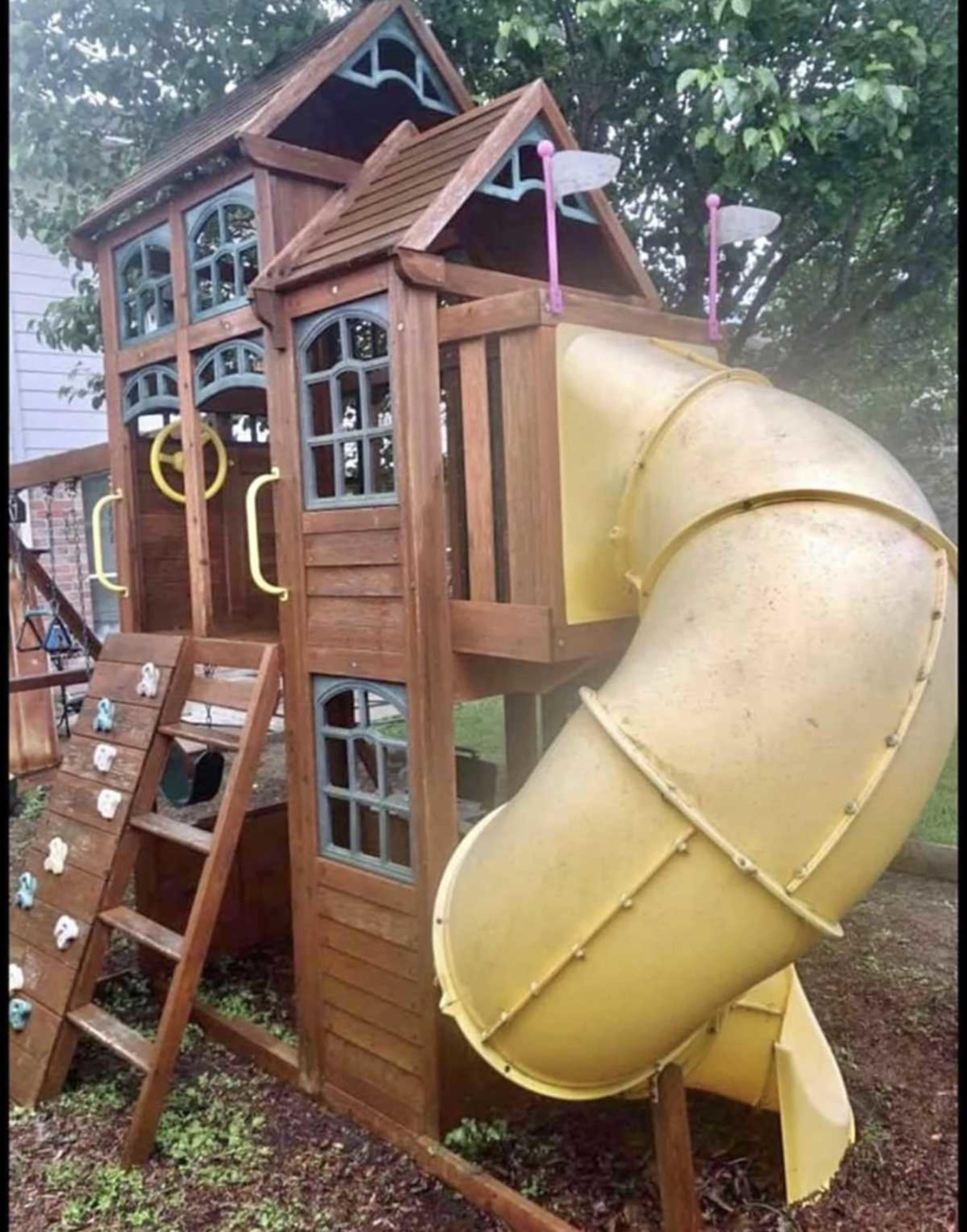 A wooden playground structure with a yellow slide, climbing wall, and two playhouses.