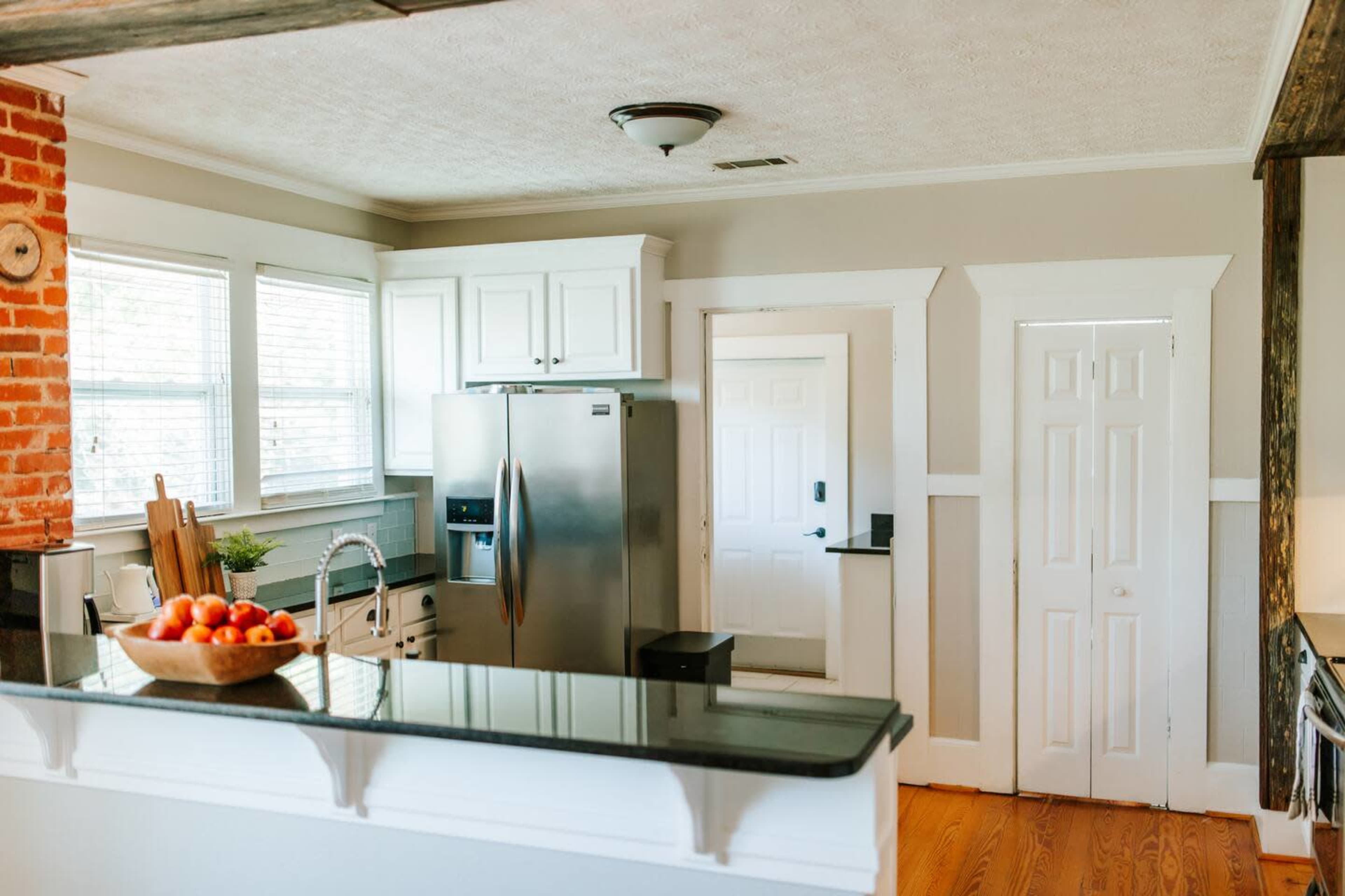 The image shows a modern kitchen featuring stainless steel appliances, white cabinetry, and hardwood flooring.