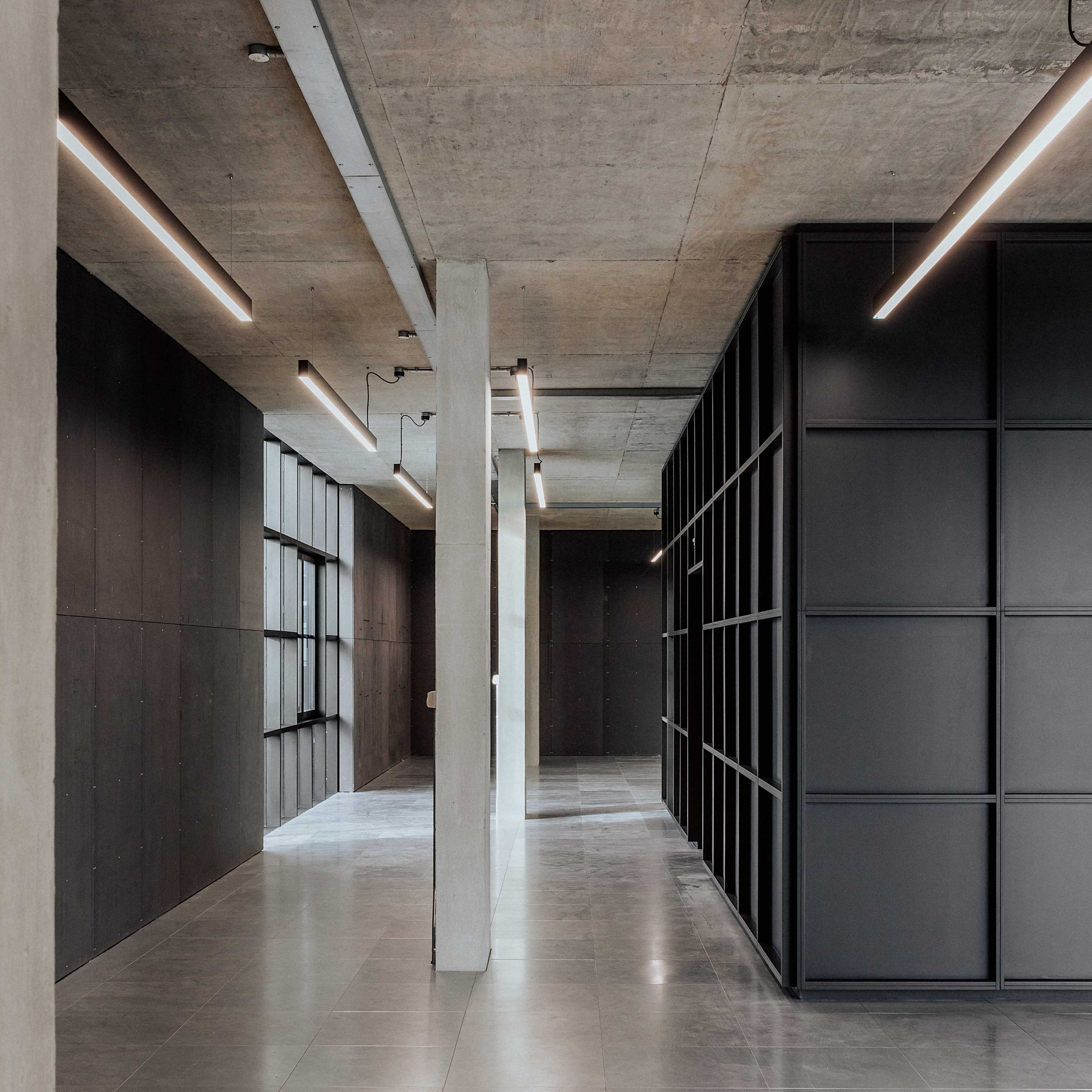 The image shows a modern interior space with concrete walls, polished tile flooring, and linear lighting fixtures.