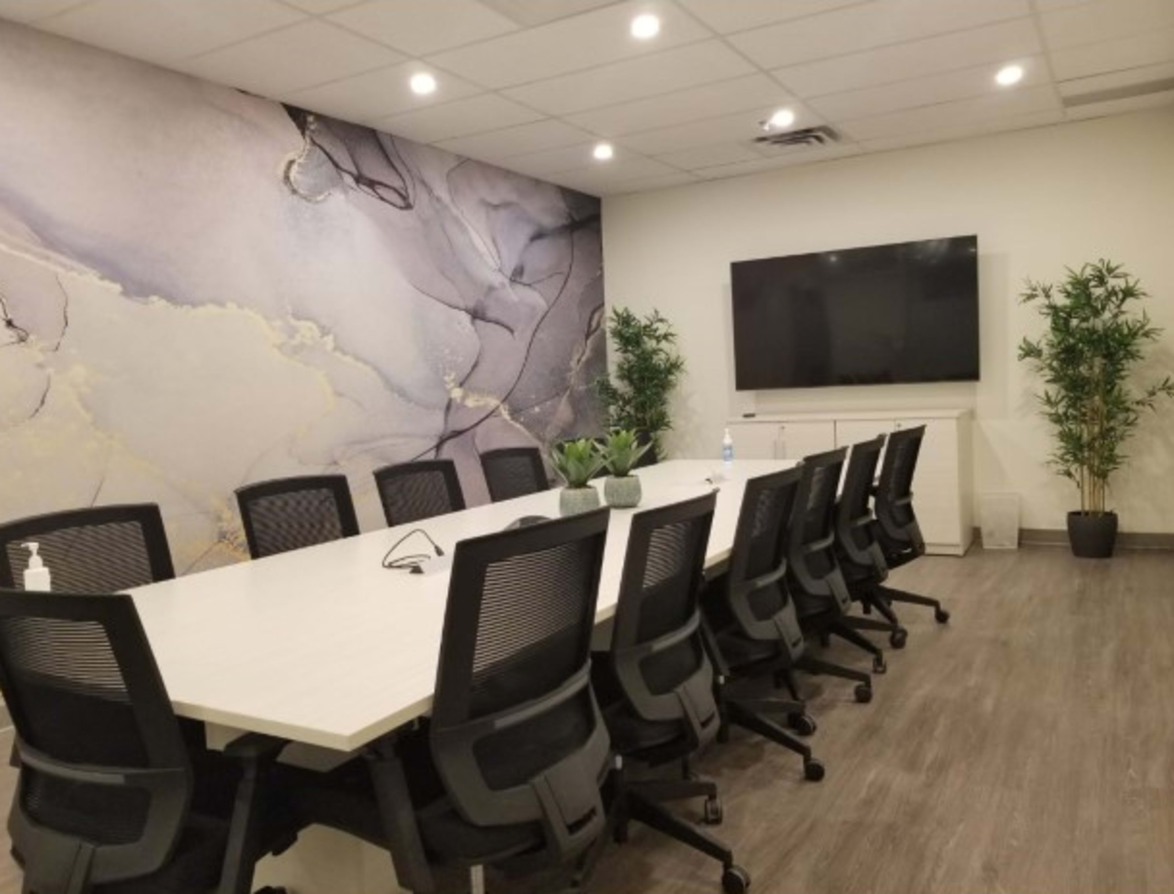 A modern conference room featuring a long white table surrounded by black ergonomic chairs, a large wall-mounted screen, and a decorative wall with abstract patterns.
