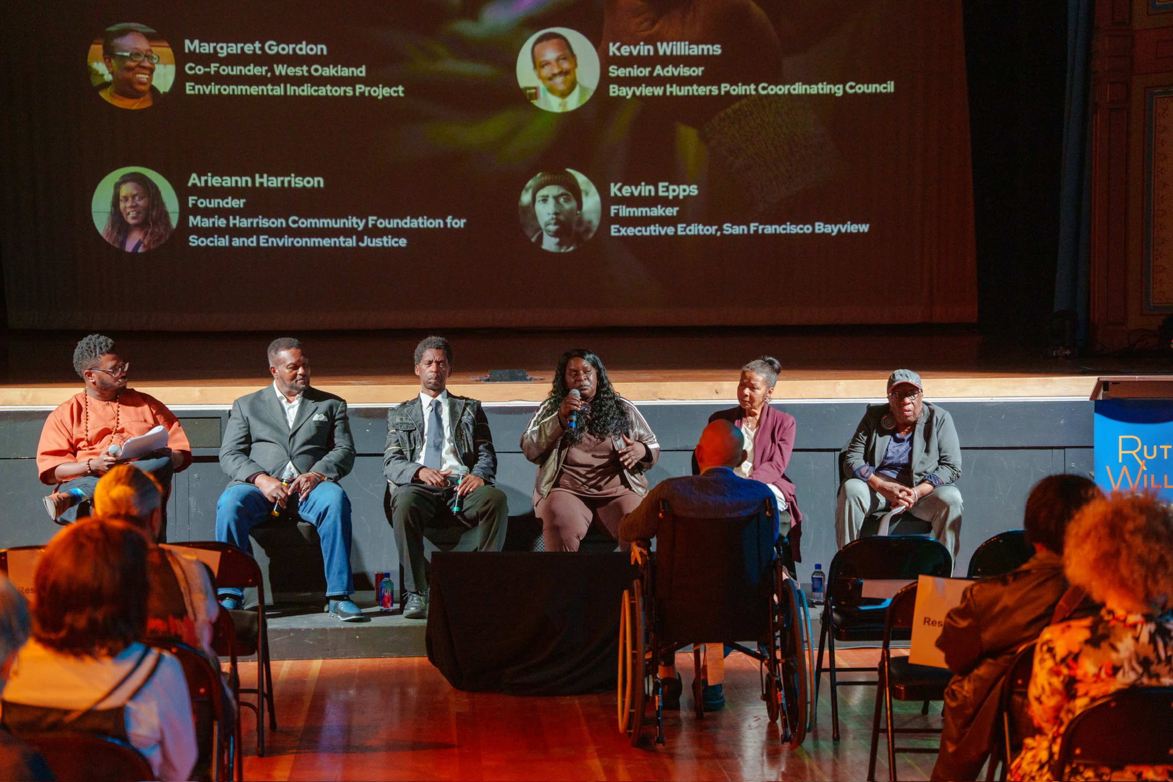 A panel discussion featuring various speakers, including Margaret Gordon and Kevin Epps, takes place on a stage with a large projection behind them.