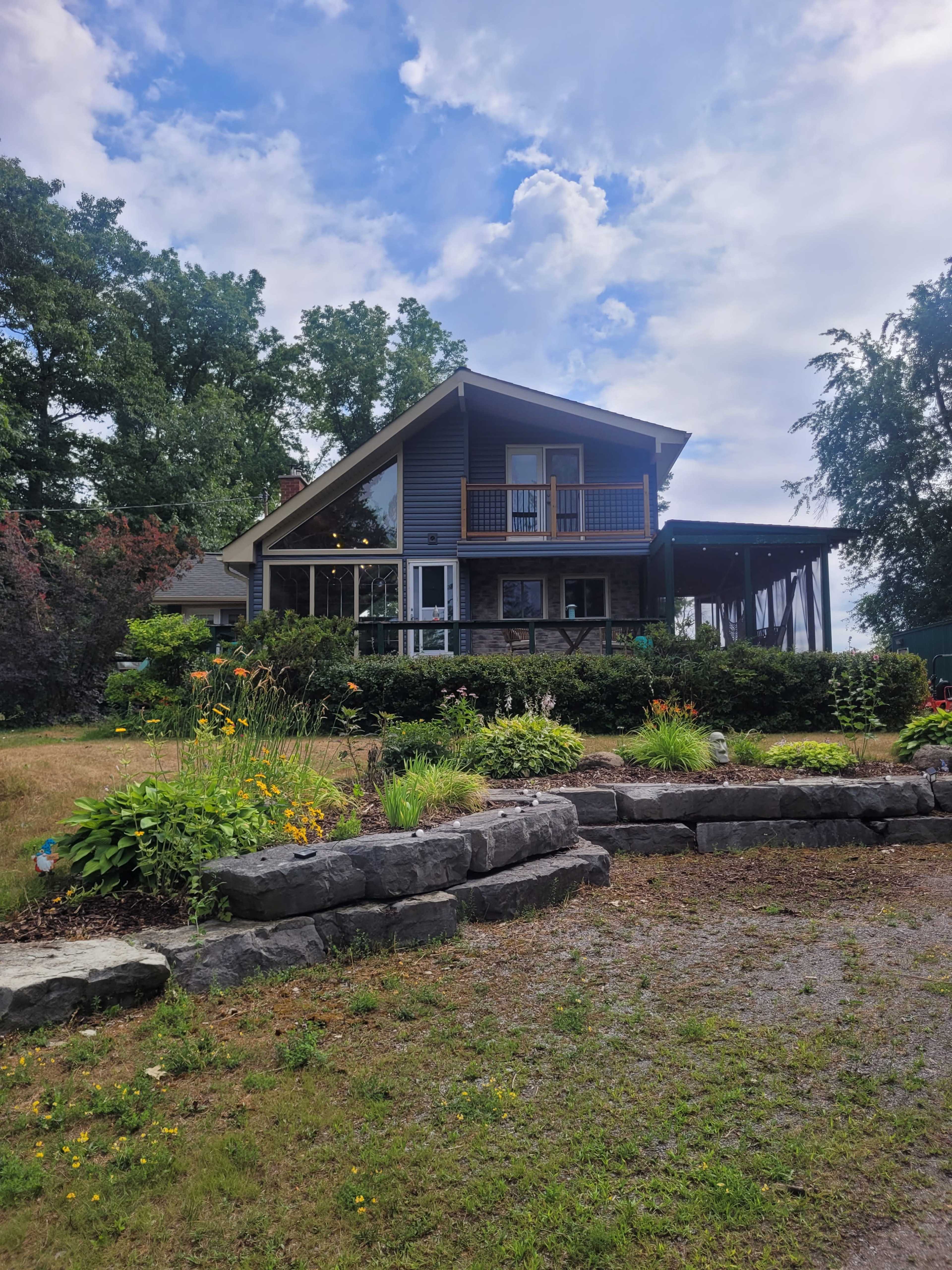 A two-story house with a large porch and surrounded by a landscaped garden featuring various flowers and greenery.