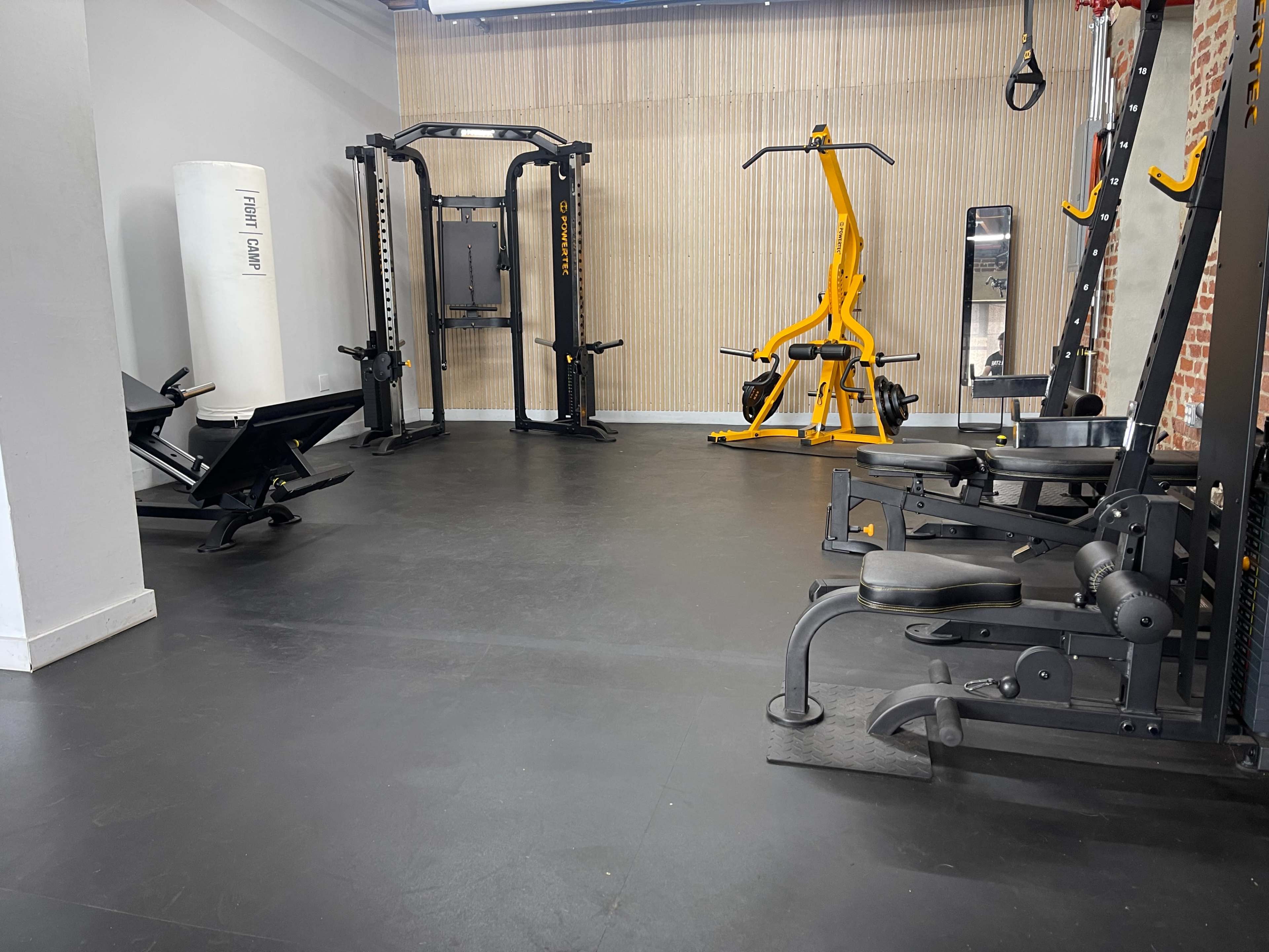 A gym interior featuring various exercise equipment, including weight machines, a punching bag, and a squat rack.