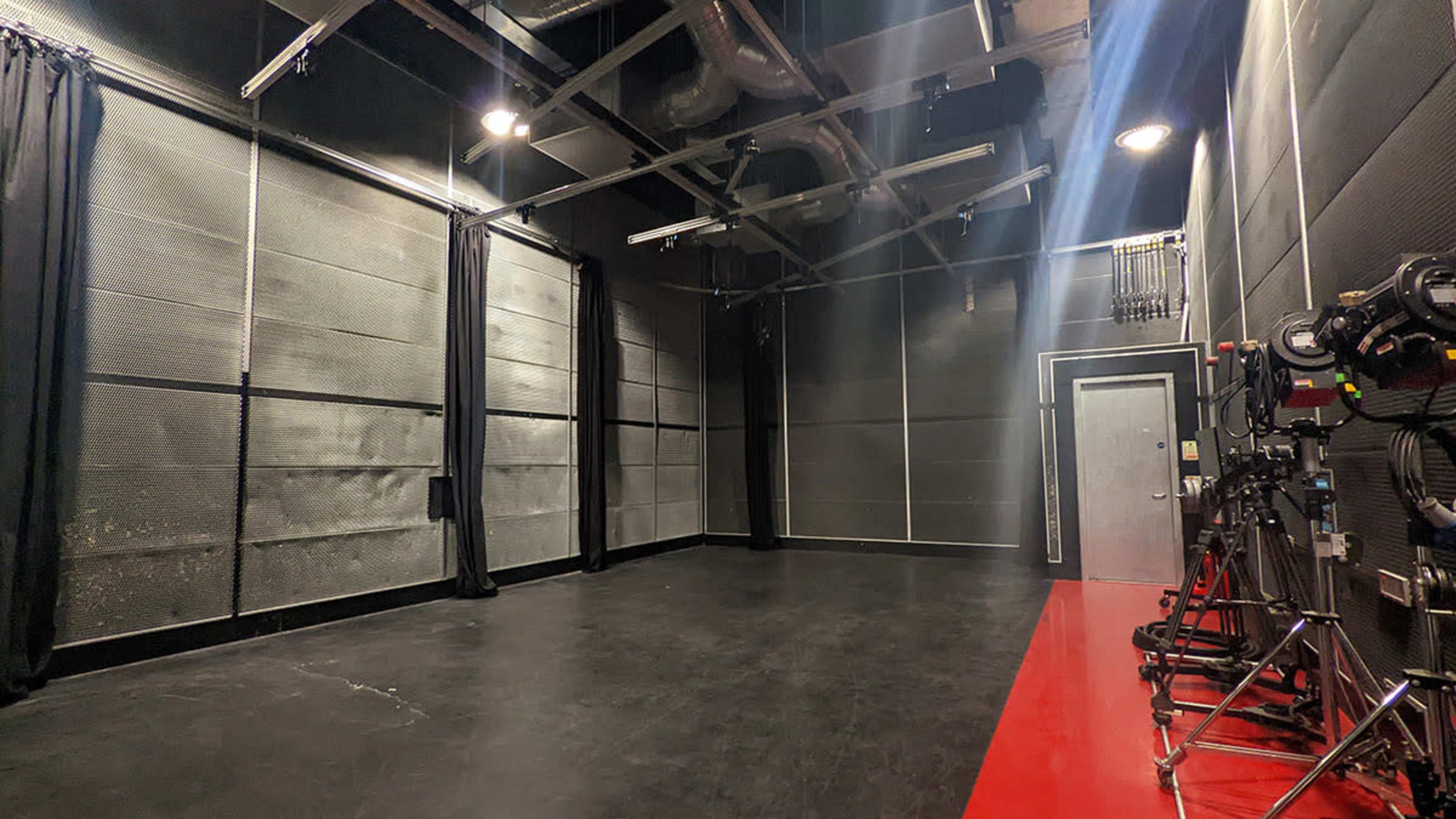 An empty black studio space with a red strip along the floor and a series of lights and equipment on the right side.