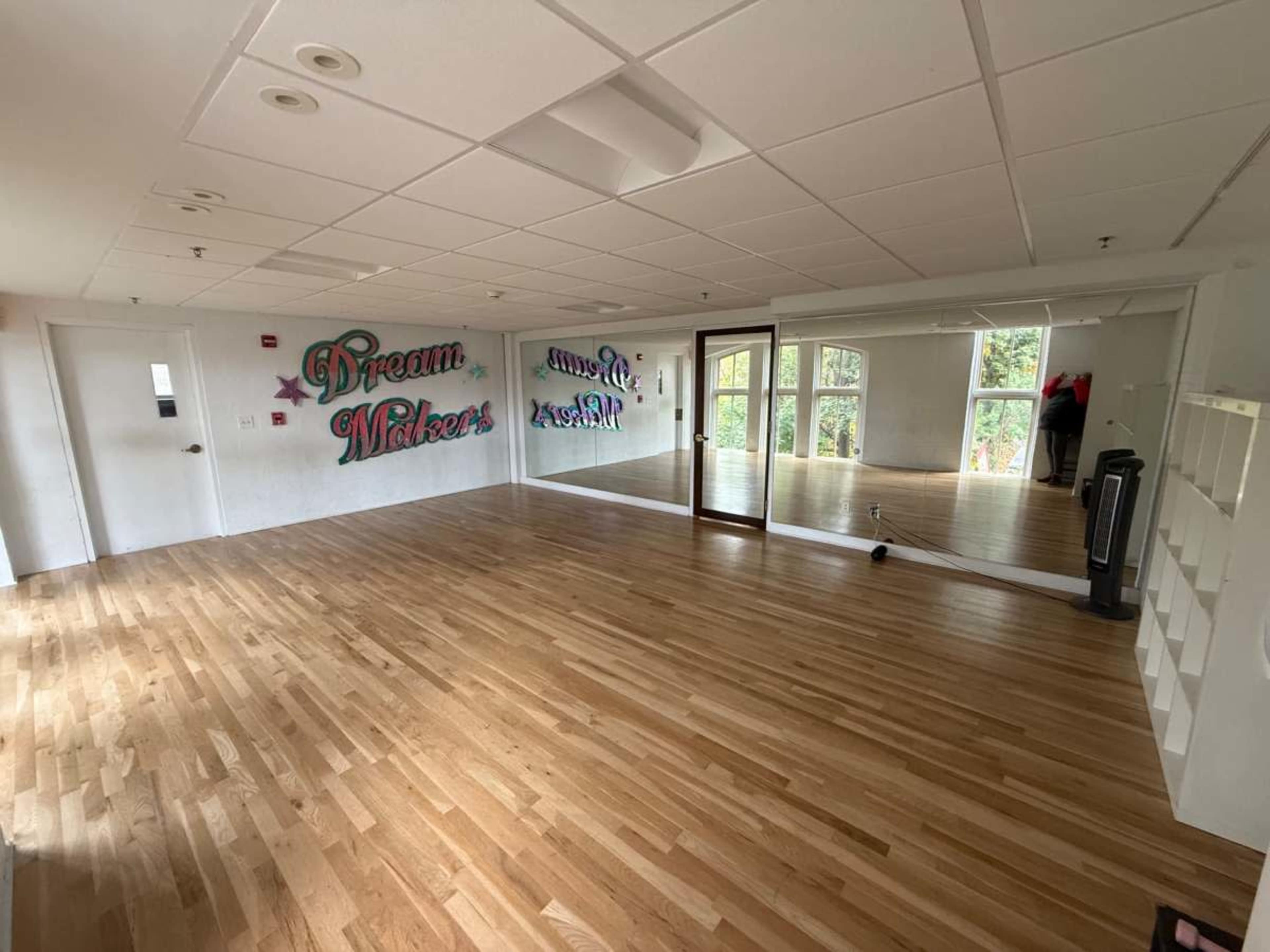 The image shows a spacious, empty room with hardwood flooring, large windows, and colorful wall murals that read "Dream" and "Make."