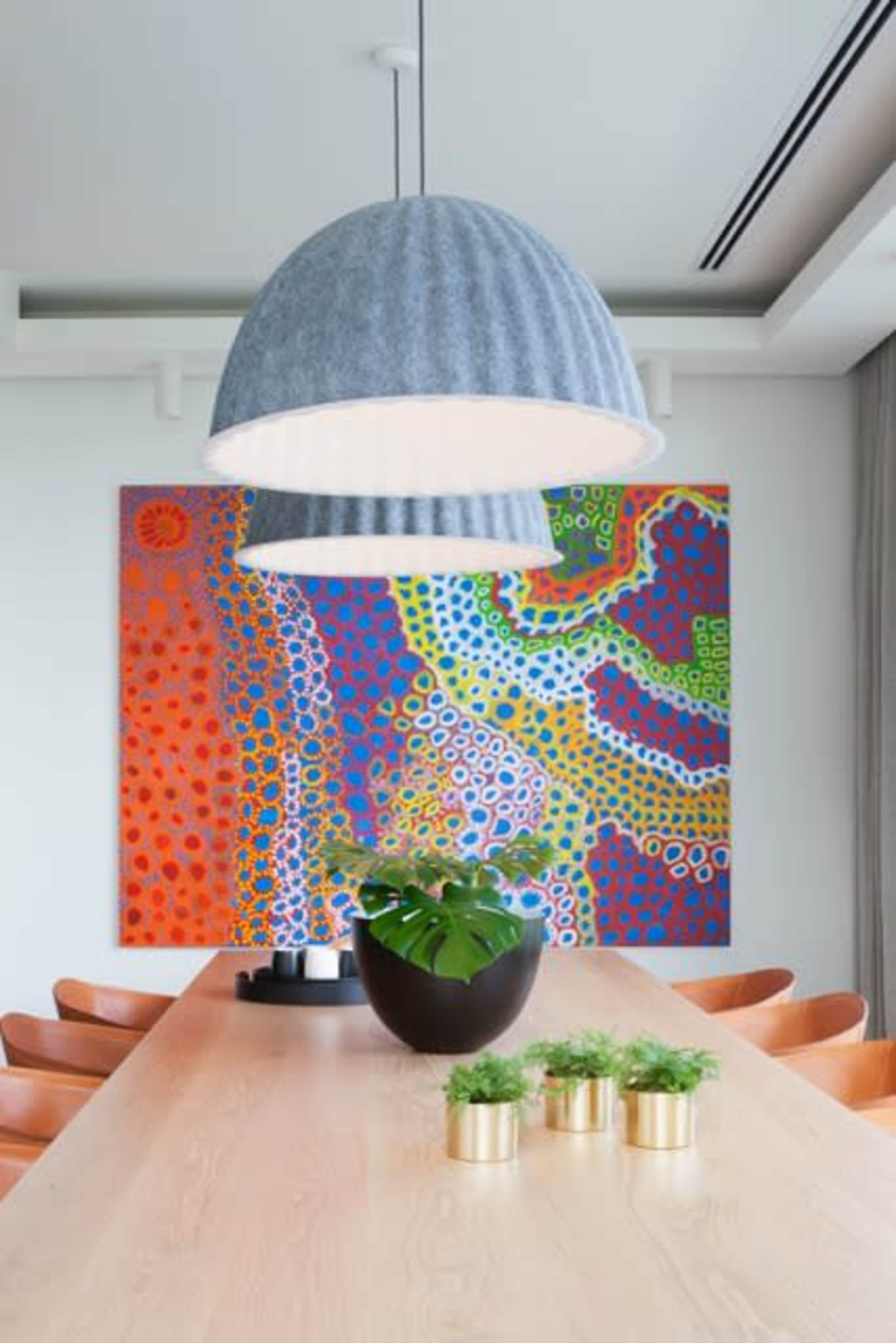 A dining table with a light gray pendant lamp and a colorful abstract painting is set against a wall, featuring a potted plant and small planters with greenery on the table.