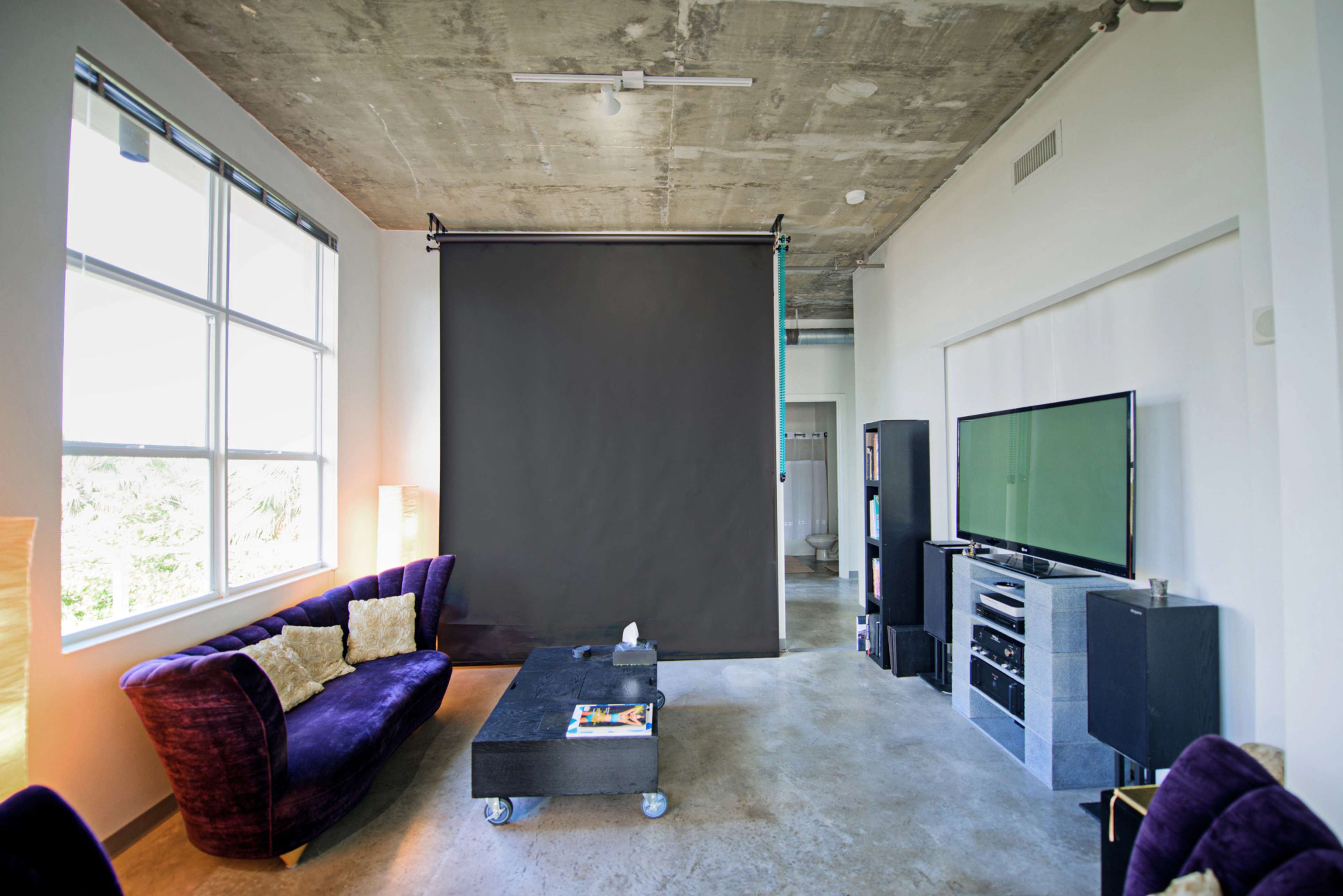 A modern living room features a purple sofa, a black curtain backdrop, and a television mounted on a gray media console.