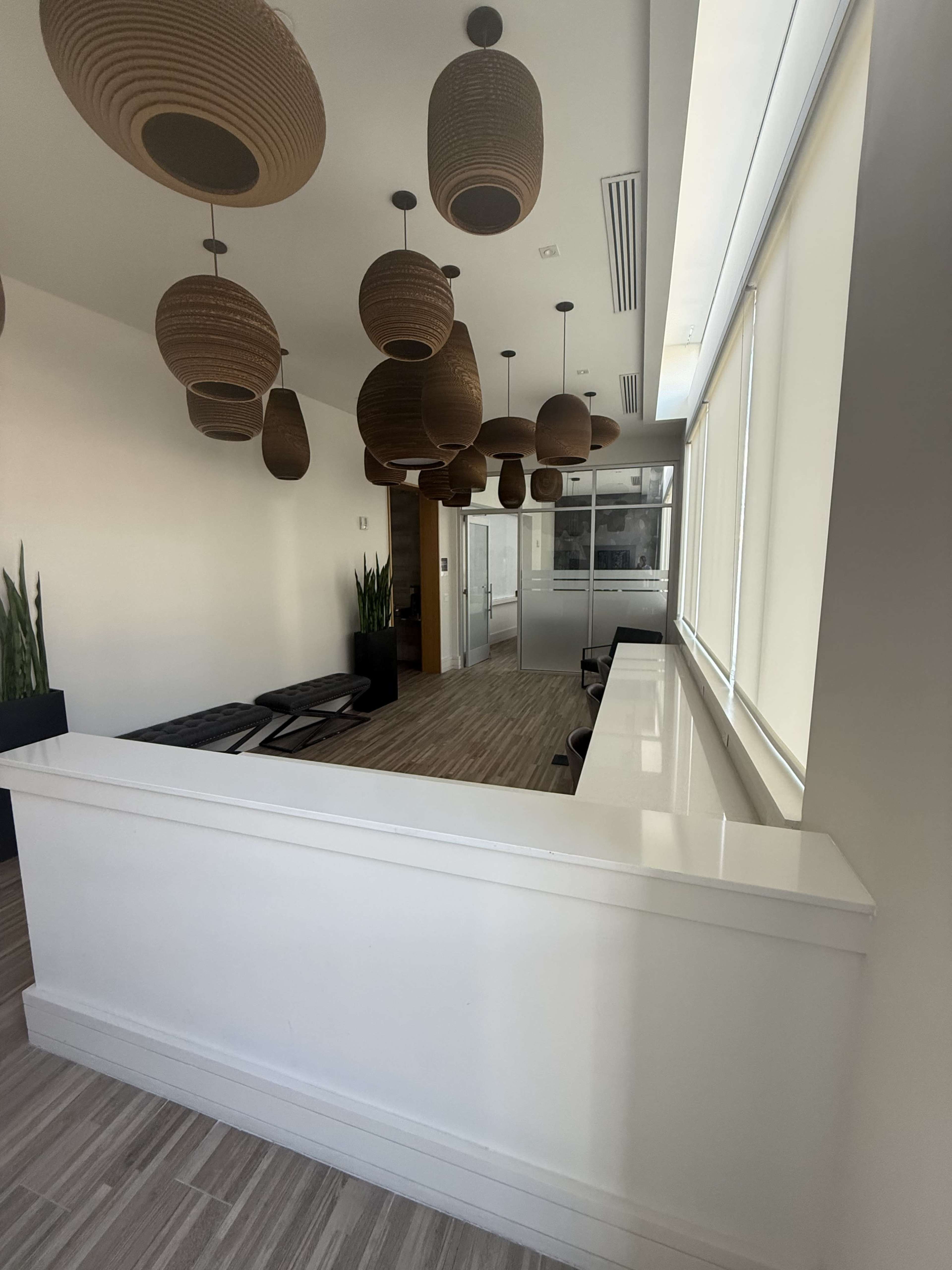 The image shows a modern lobby area with hanging light fixtures, a white reception counter, and seating arrangements in a minimalist design.