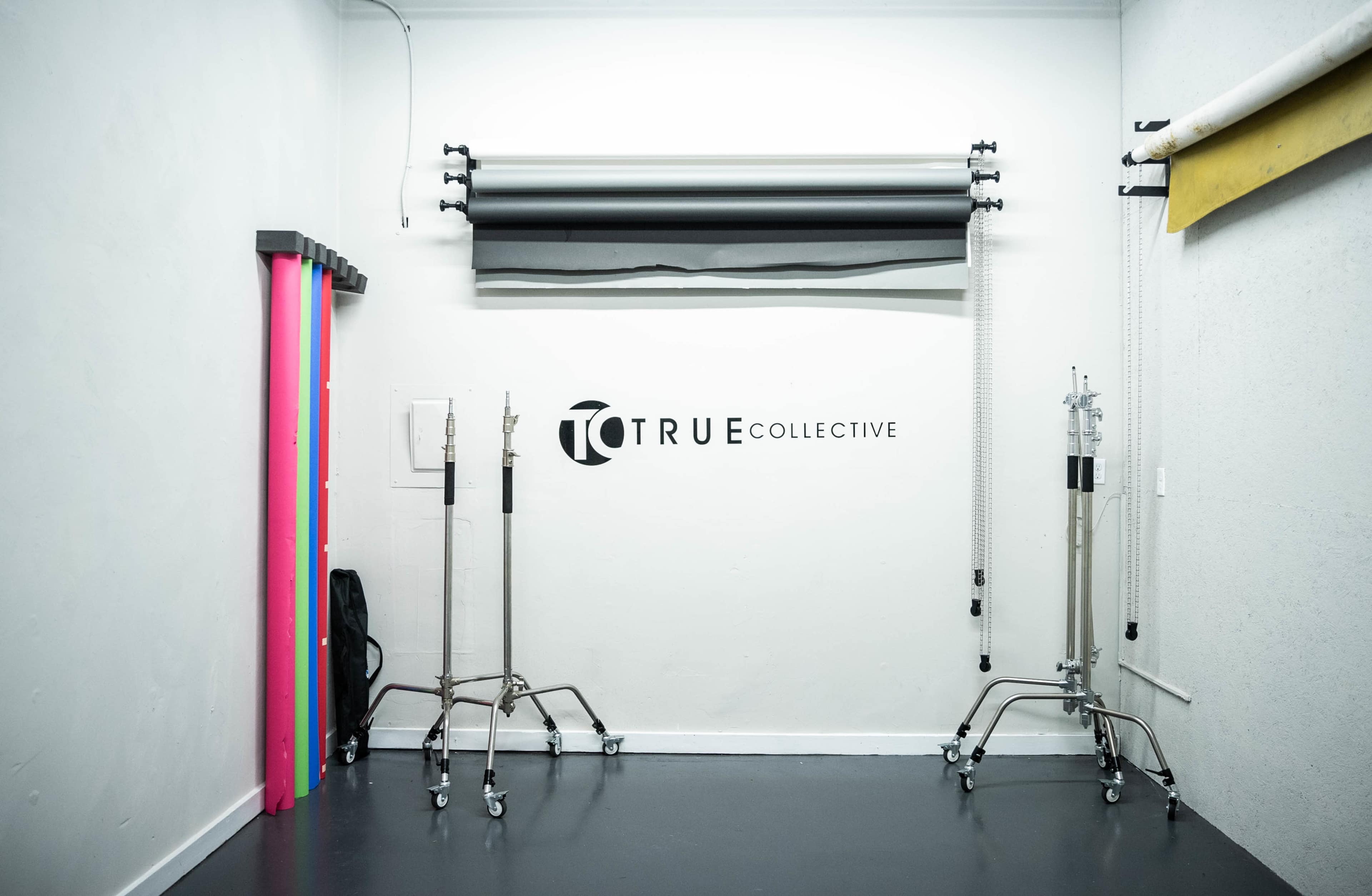 A studio space featuring a wall with the text "TRUE COLLECTIVE," several background roll paper colors, and equipment stands.