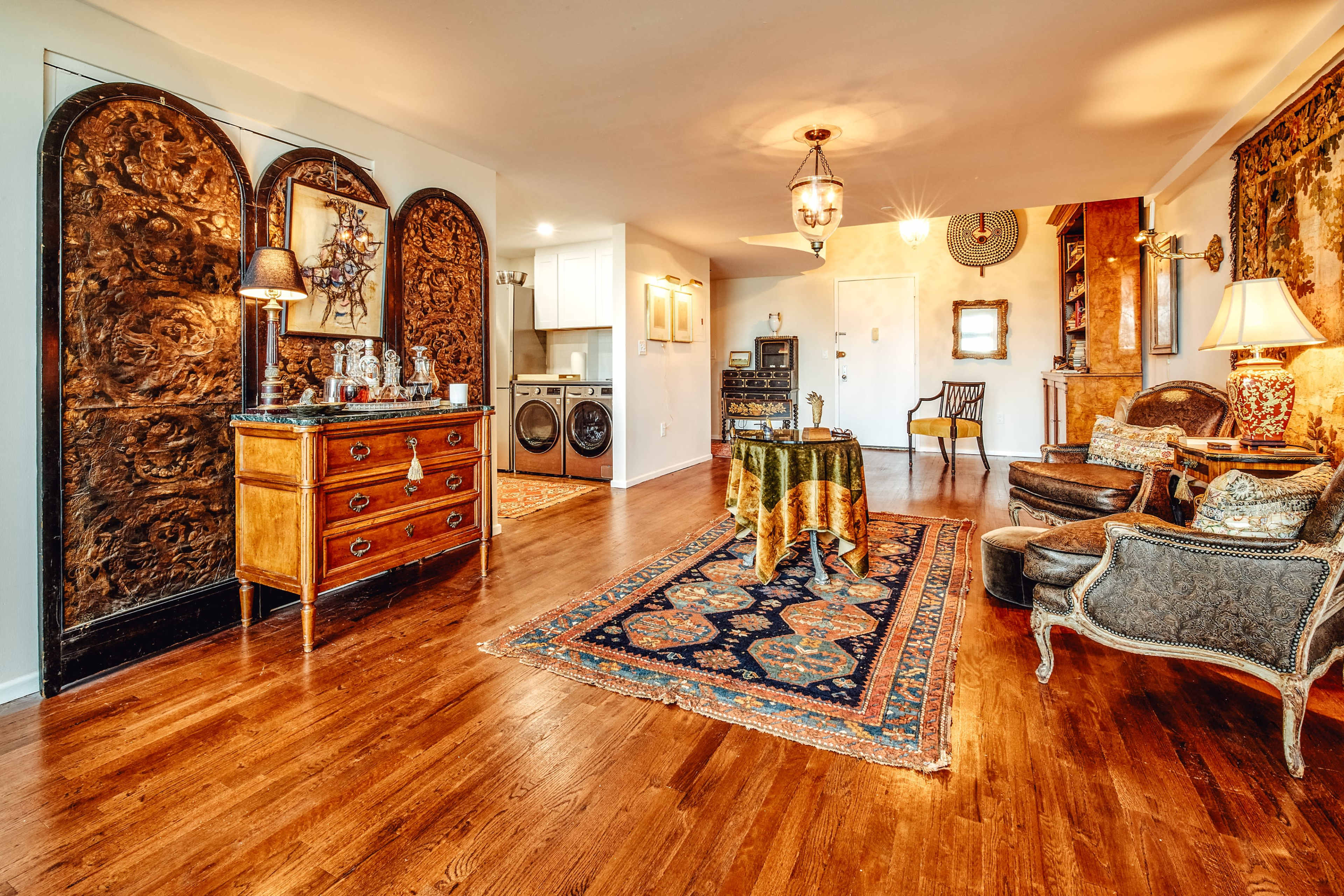 A spacious living area with hardwood floors, a decorative rug, vintage furniture, and ornate wall decorations.