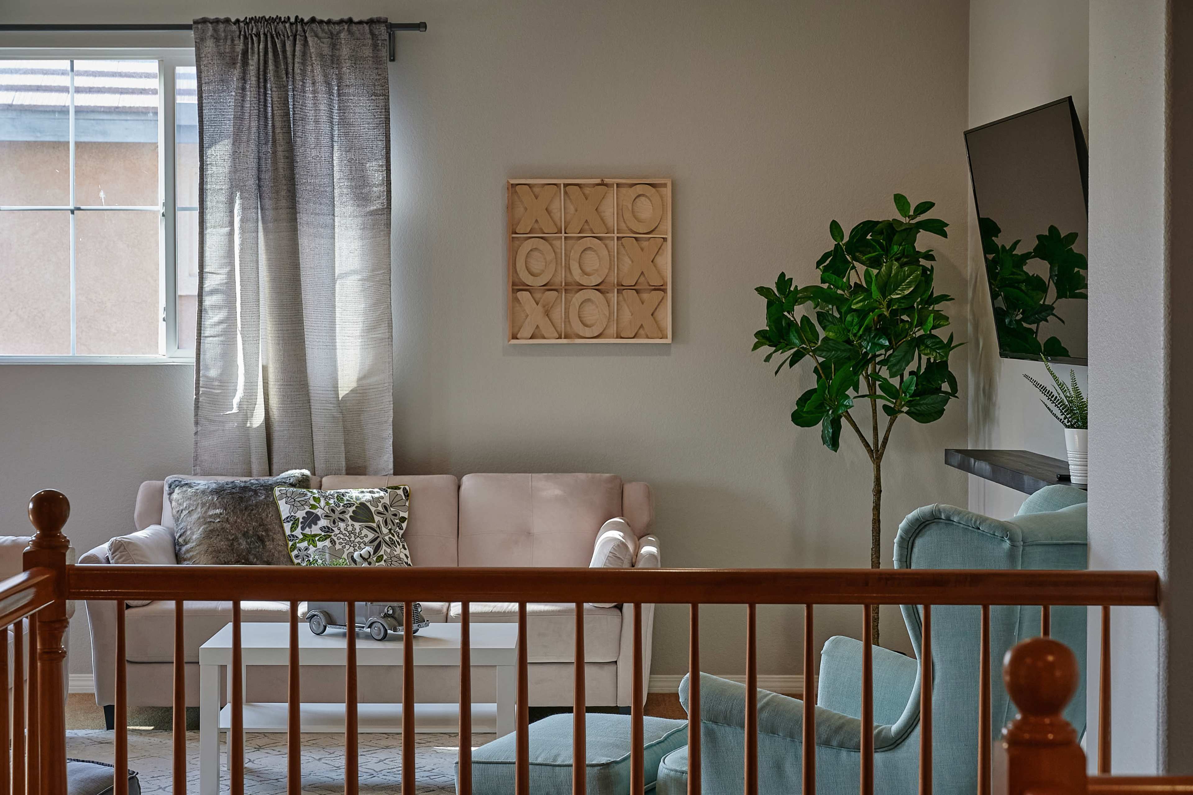 A cozy living room with a light-colored sofa, a coffee table, a potted plant, and a window with sheer curtains.