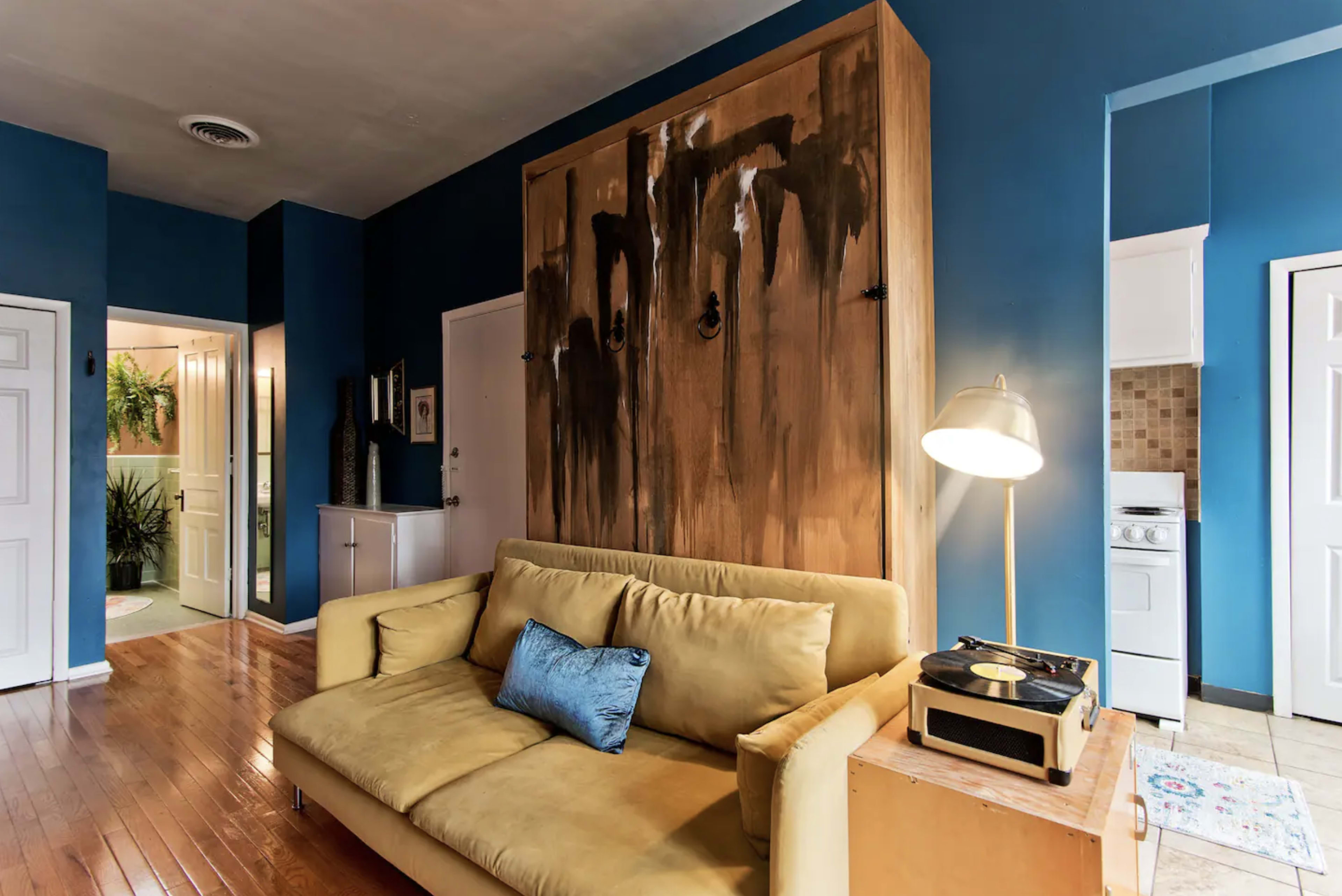 A living area featuring a yellow sofa, a wooden cabinet with an abstract design, and a standing lamp beside a record player.