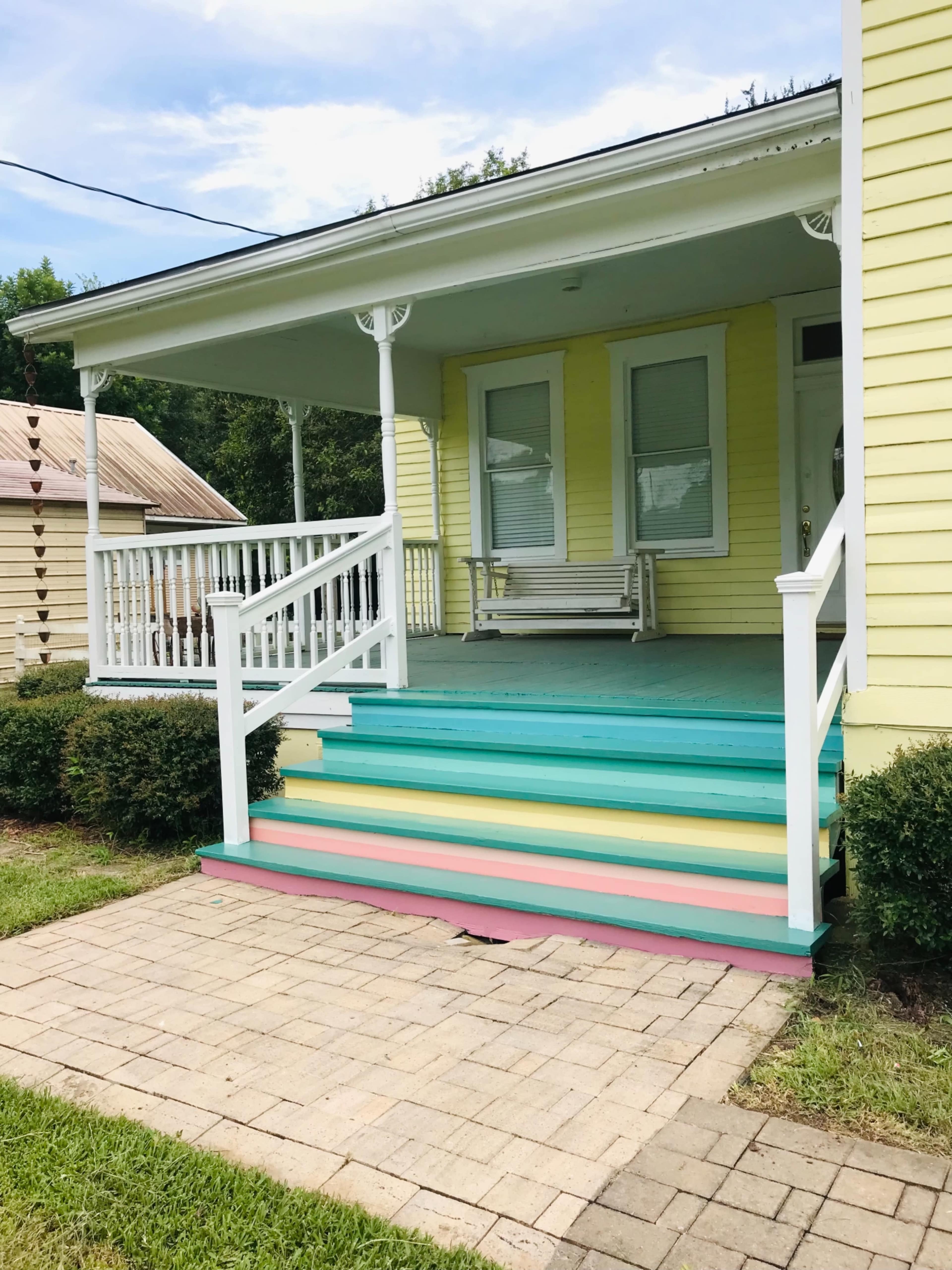 A yellow house with a front porch featuring multicolored steps, flanked by neatly trimmed hedges.