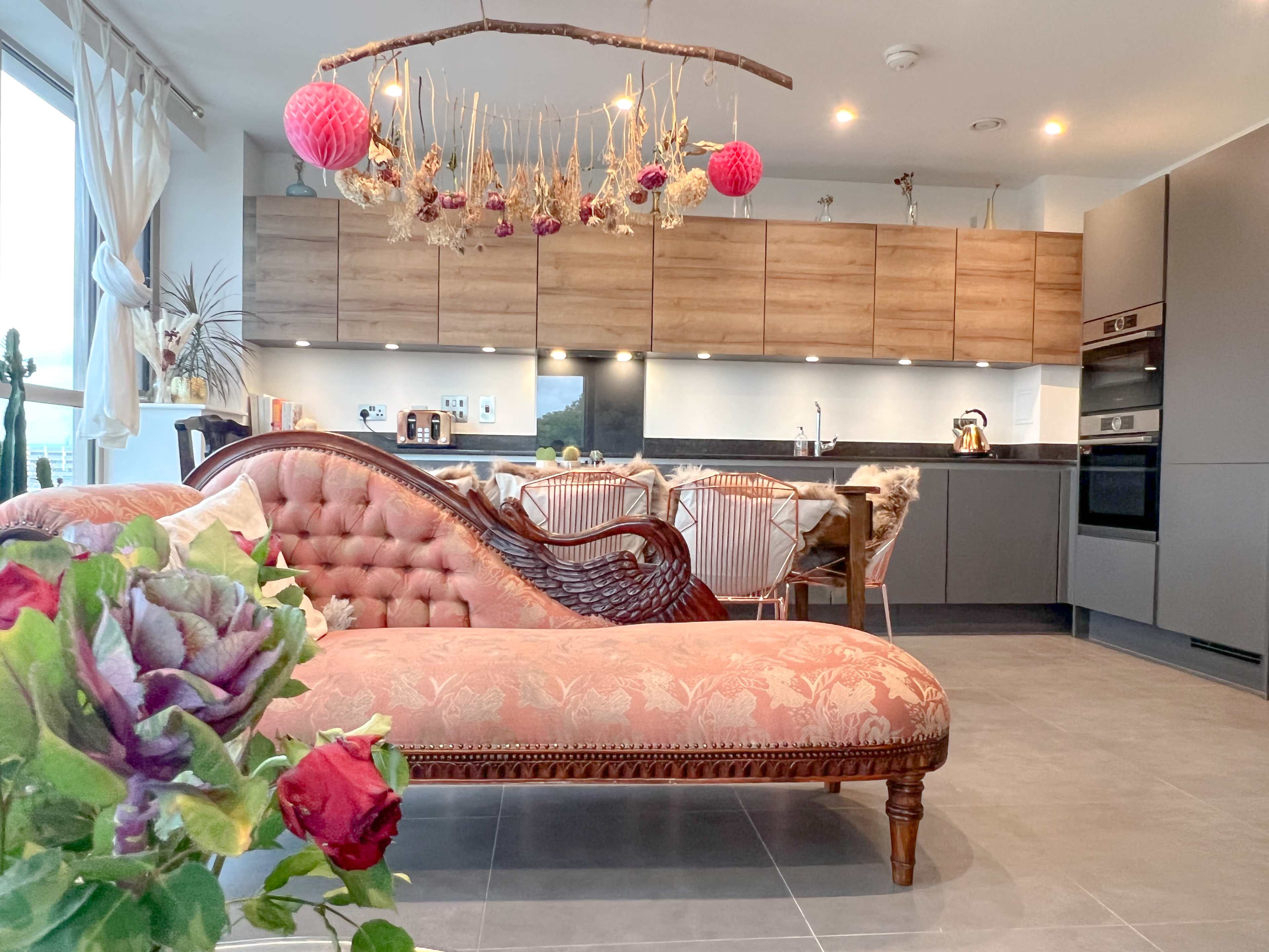 A modern kitchen with wooden cabinets and a decorated living area featuring a vintage-style sofa and hanging decor.