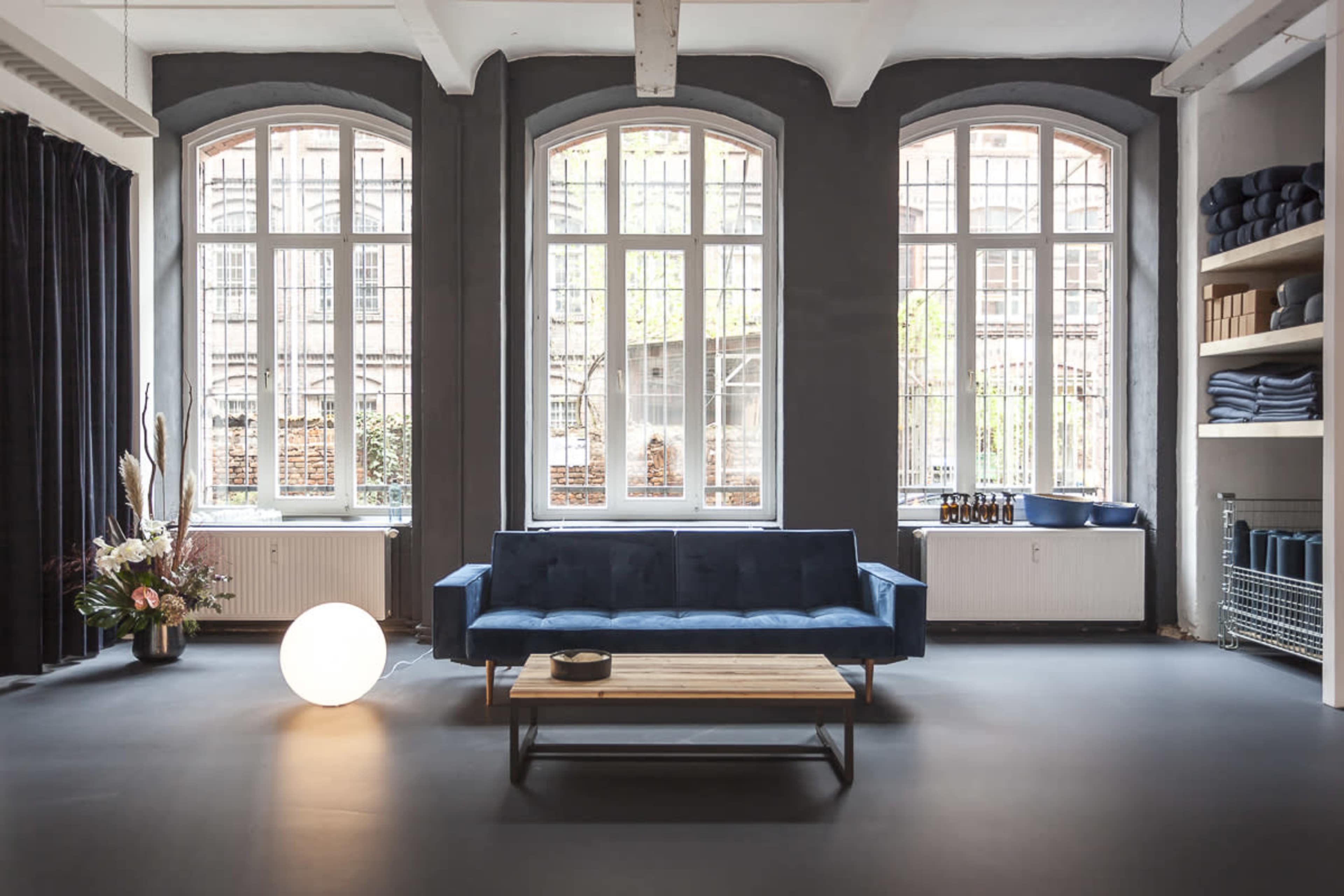 A modern, minimalist room features a blue sofa and a wooden coffee table, with large windows letting in natural light.