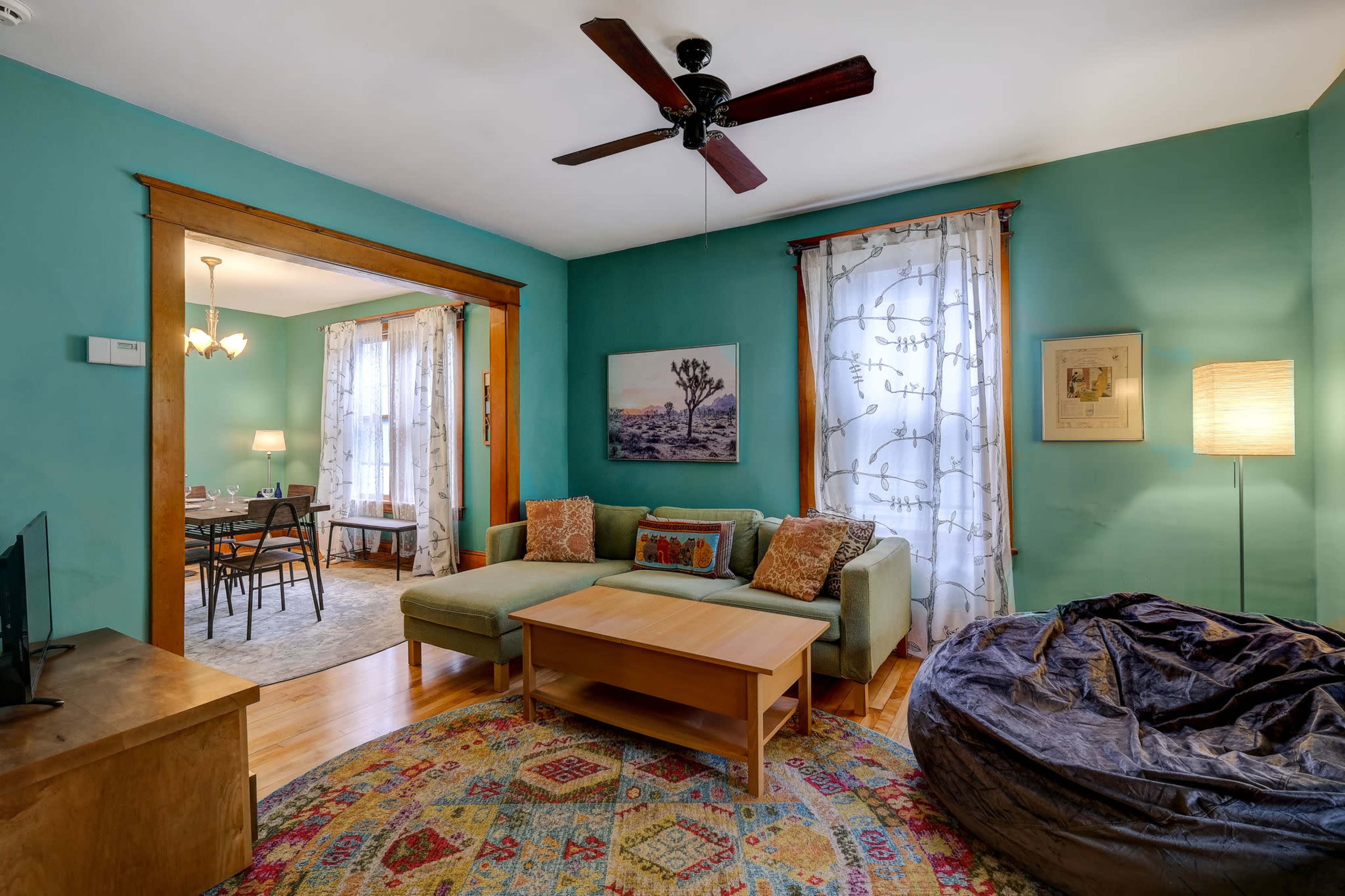 The room features a green-painted wall with a couch and a coffee table, framed by a doorway leading to a dining area.