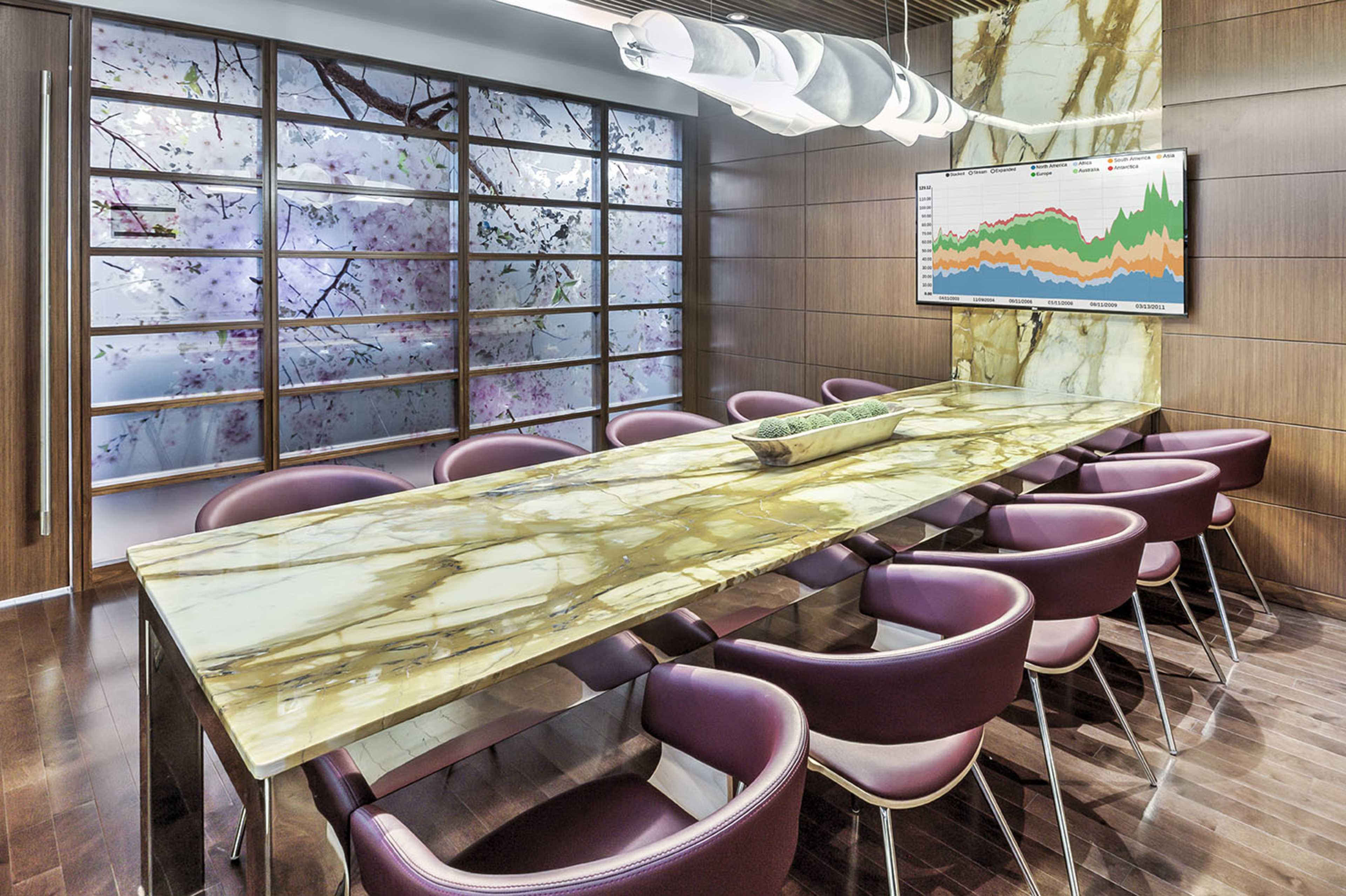 A modern conference room features a large marble table surrounded by purple chairs, with a floral-patterned backdrop and a graph displayed on the wall.