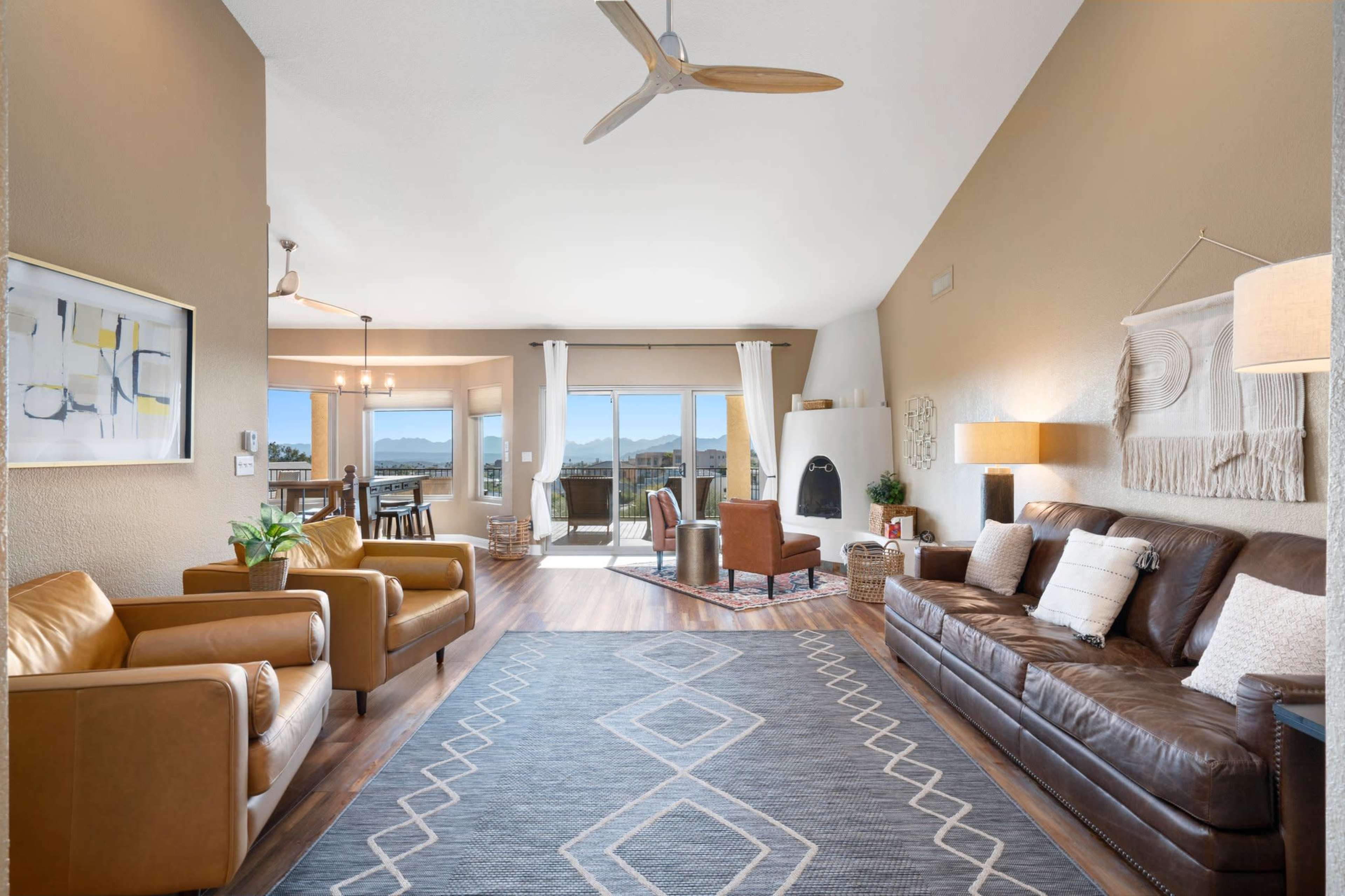 A modern living room with two leather armchairs and a brown leather sofa, a patterned rug on the wooden floor, and large windows revealing a scenic view.