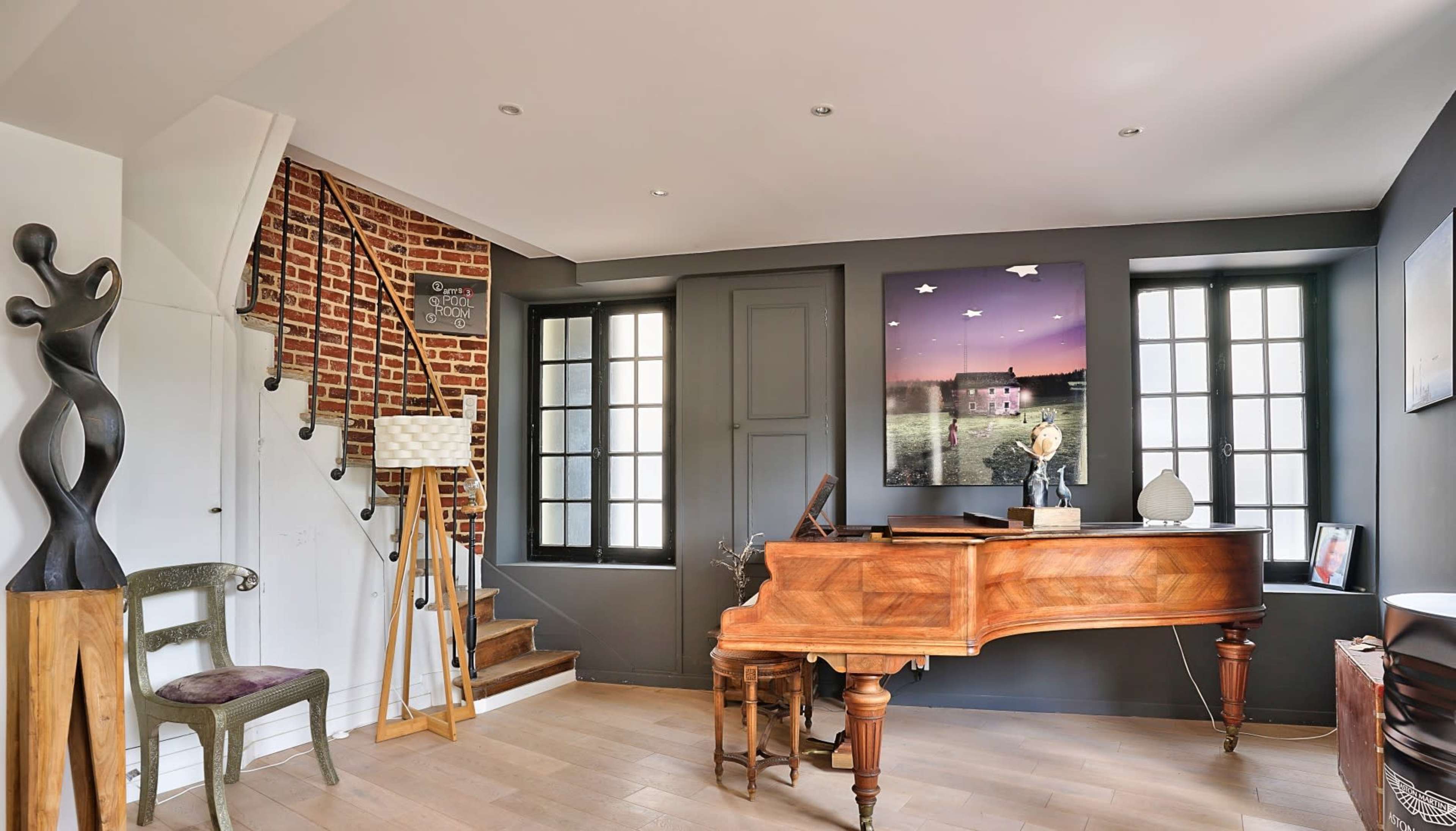A modern interior featuring a wooden grand piano, a decorative sculpture, and a staircase leading to an upper level.