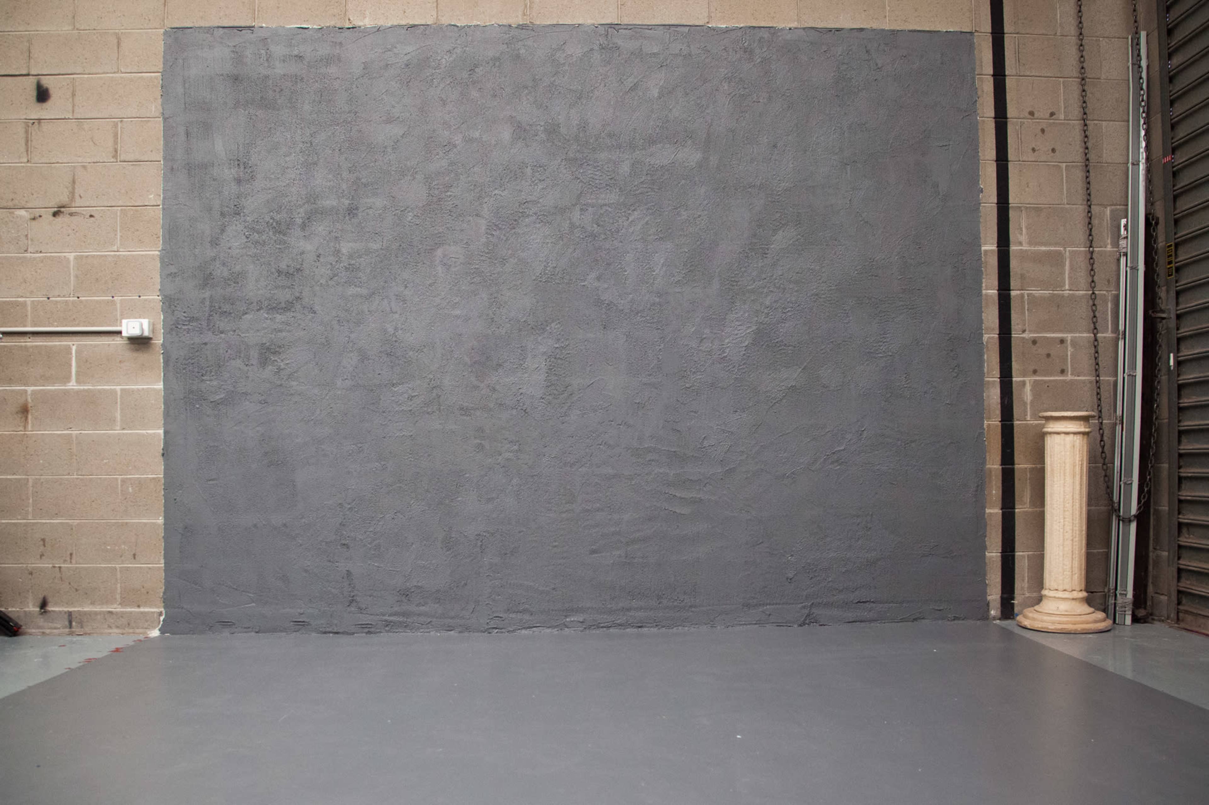 A gray textured wall in an industrial space, with a column on the right side and a concrete floor.