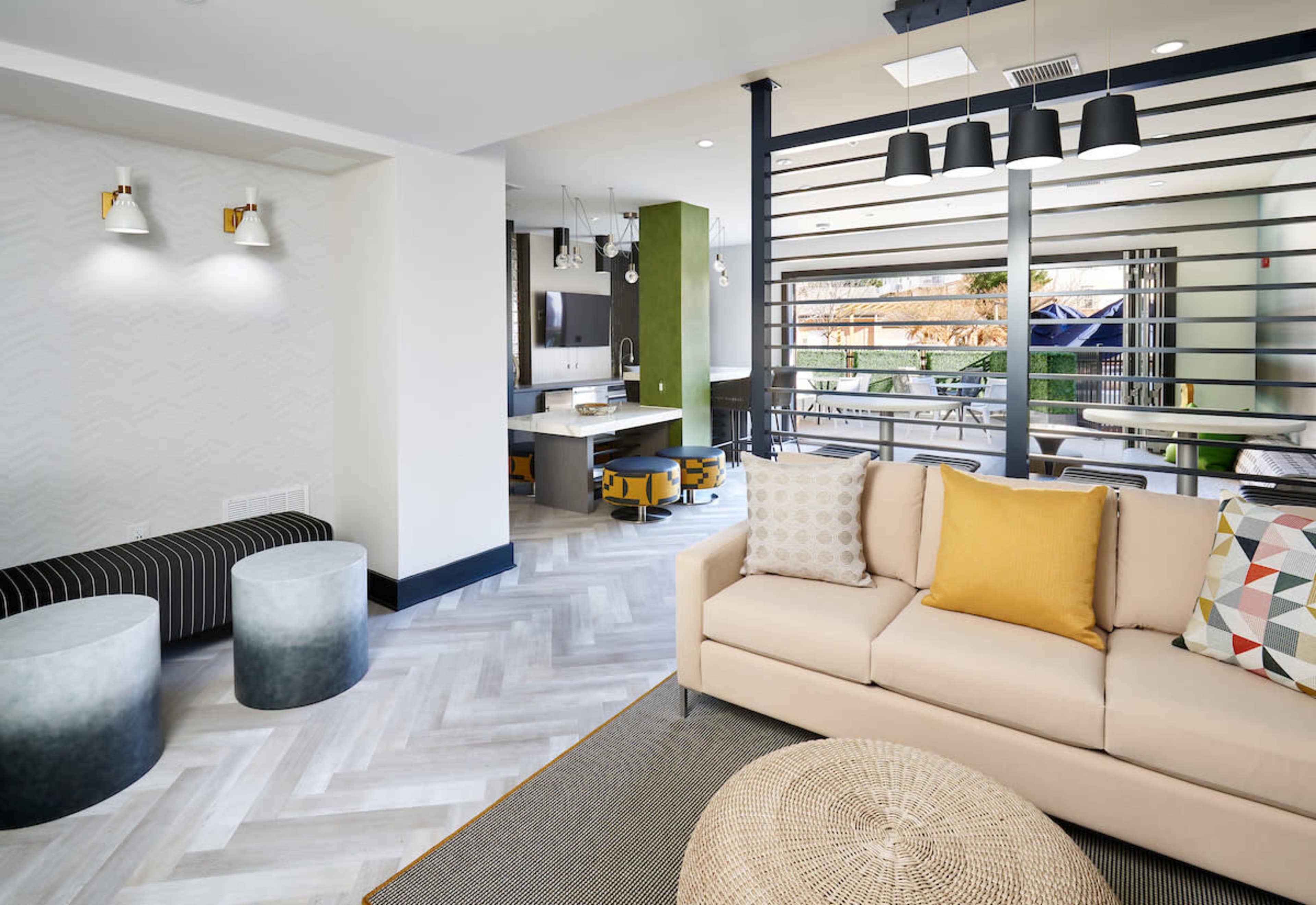 A modern lounge area with a beige sofa, geometric patterned cushions, and a view of a connected kitchen space.