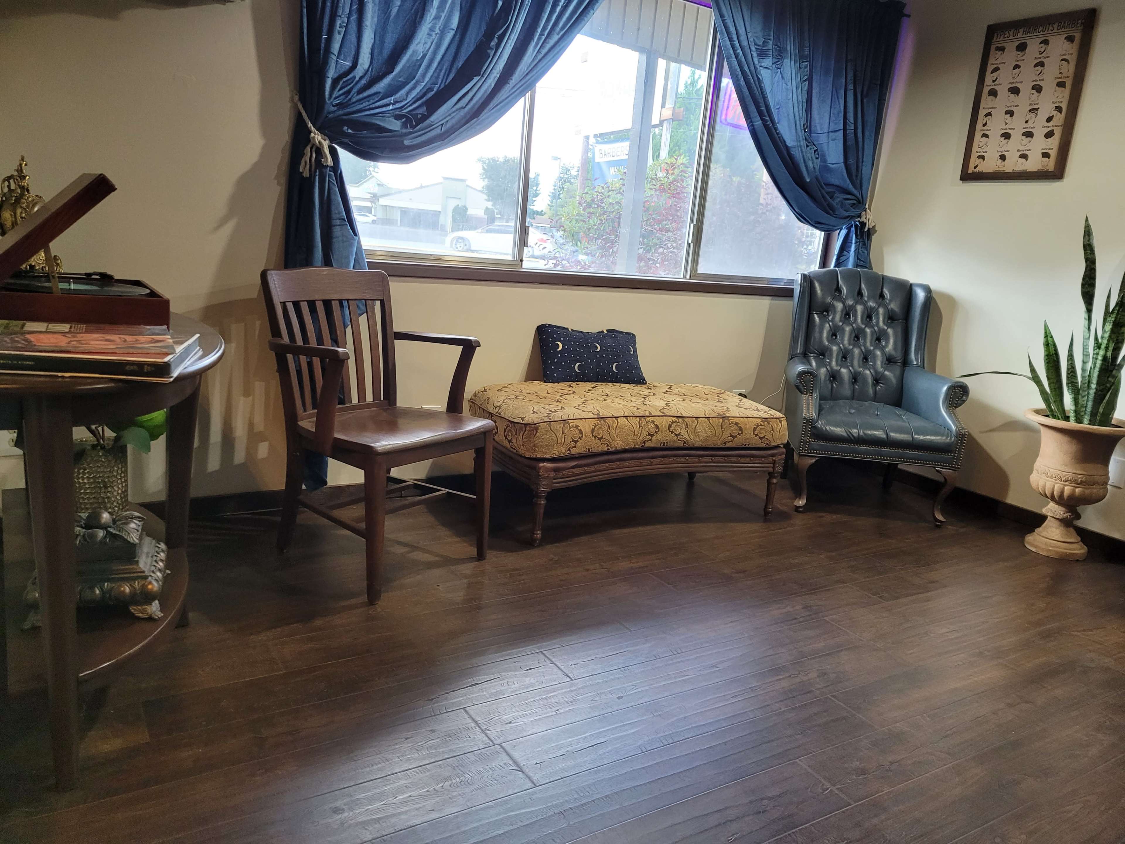 The image shows a cozy indoor seating area featuring a decorative chaise lounge, a wooden chair, a potted plant, and a window with blue drapes.