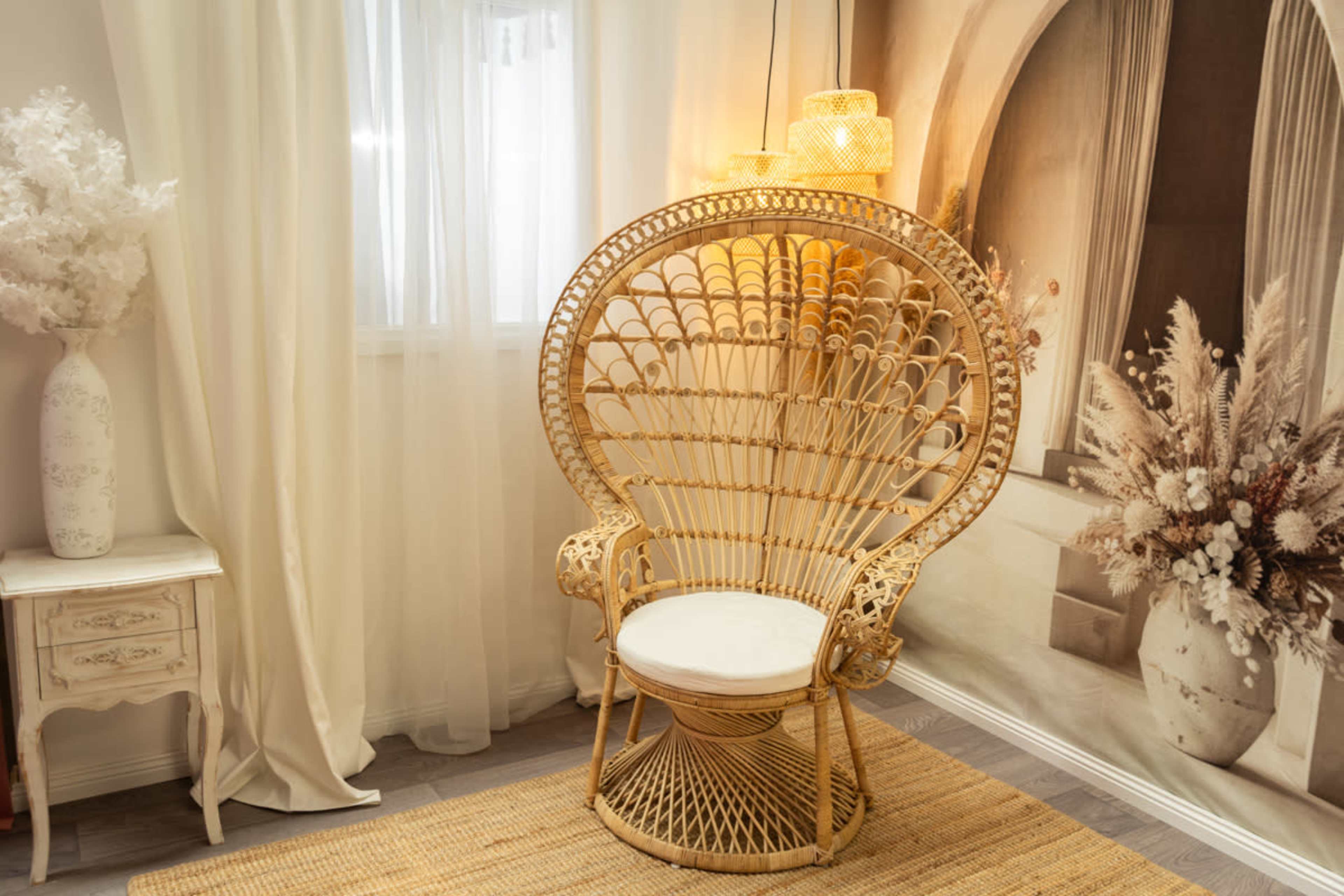 A rattan peacock chair with a cushioned seat is positioned in front of a softly lit wall featuring a decorative mural of flowers.