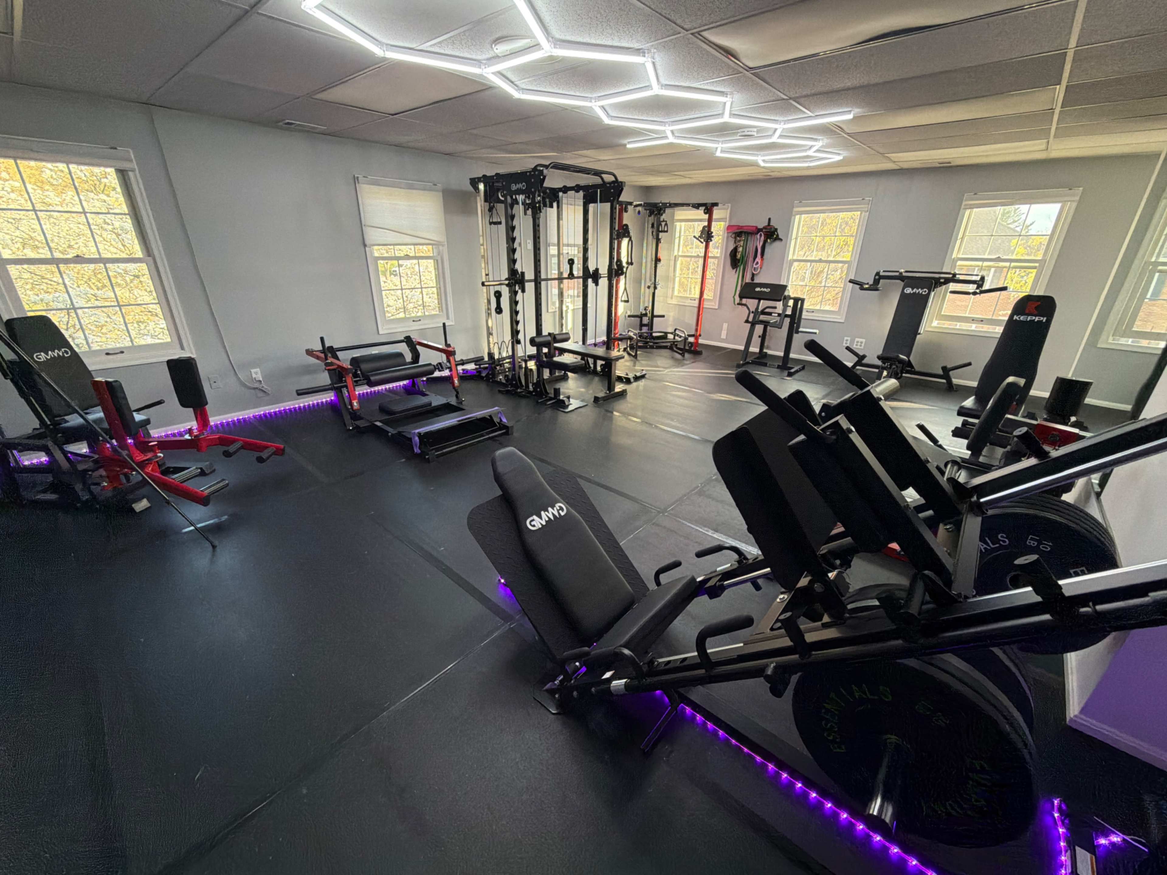 The image shows a well-equipped gym space with various weightlifting machines and benches arranged neatly on a black rubber floor.