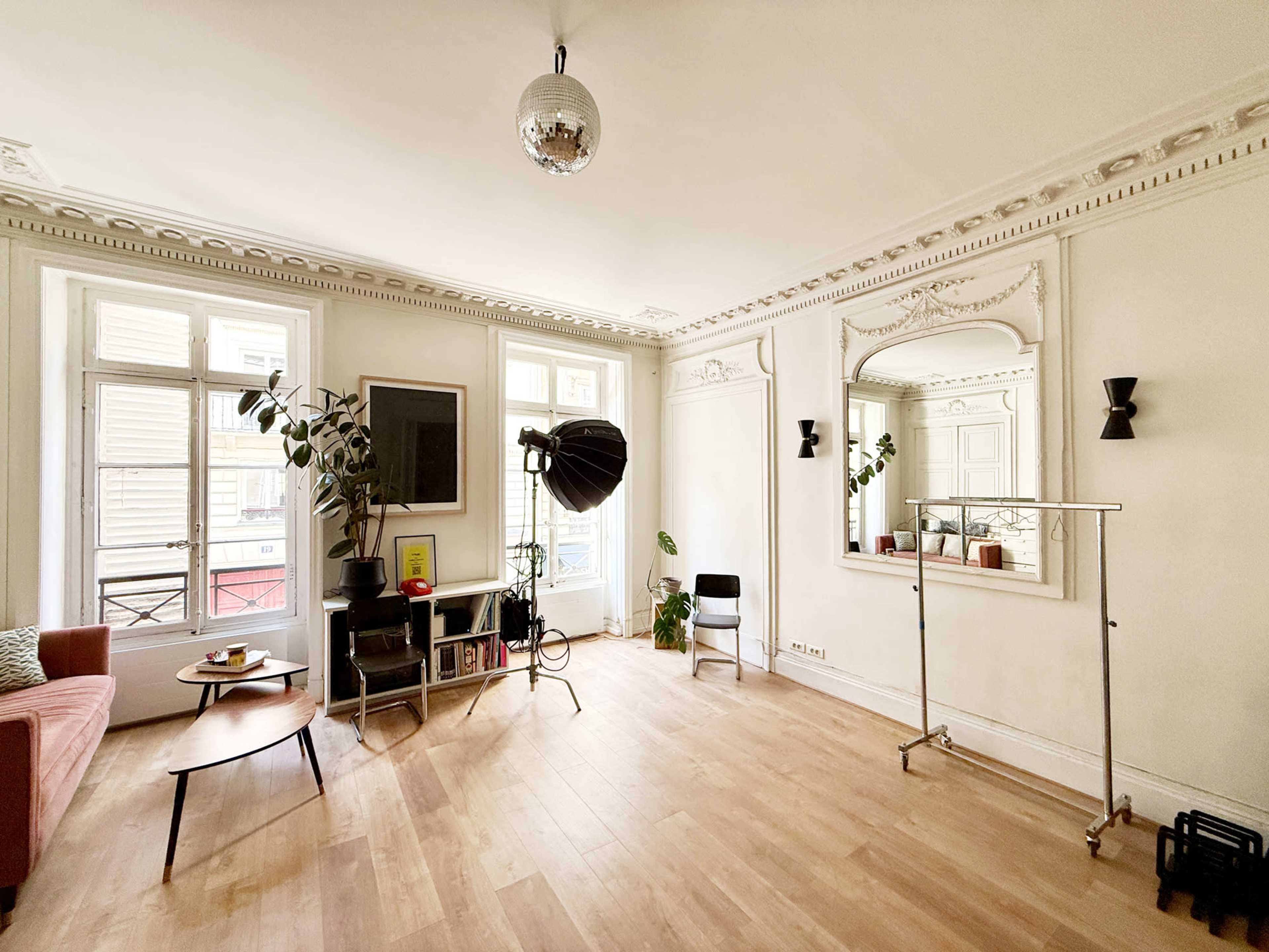 The image shows a well-lit room featuring a pink sofa, a mirror, a tall lamp, a plant, a coffee table, and a clothing rack.