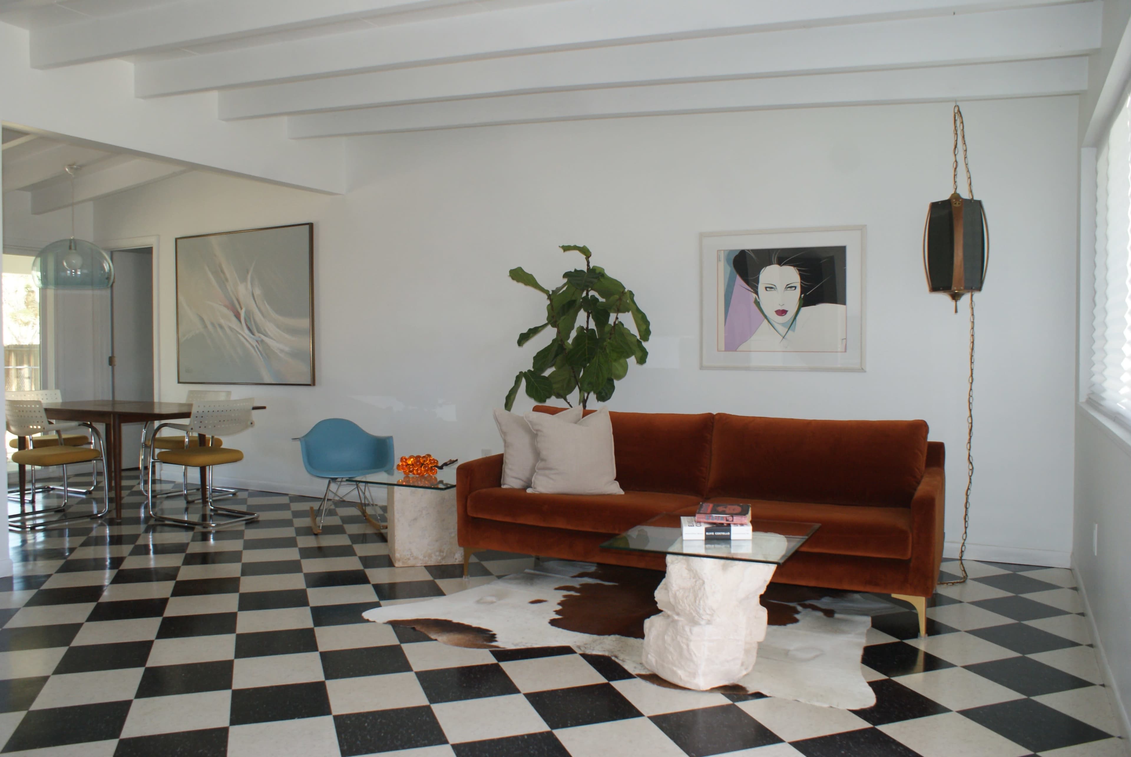 A modern living room with a brown velvet sofa, a glass coffee table, and black-and-white checkered flooring.