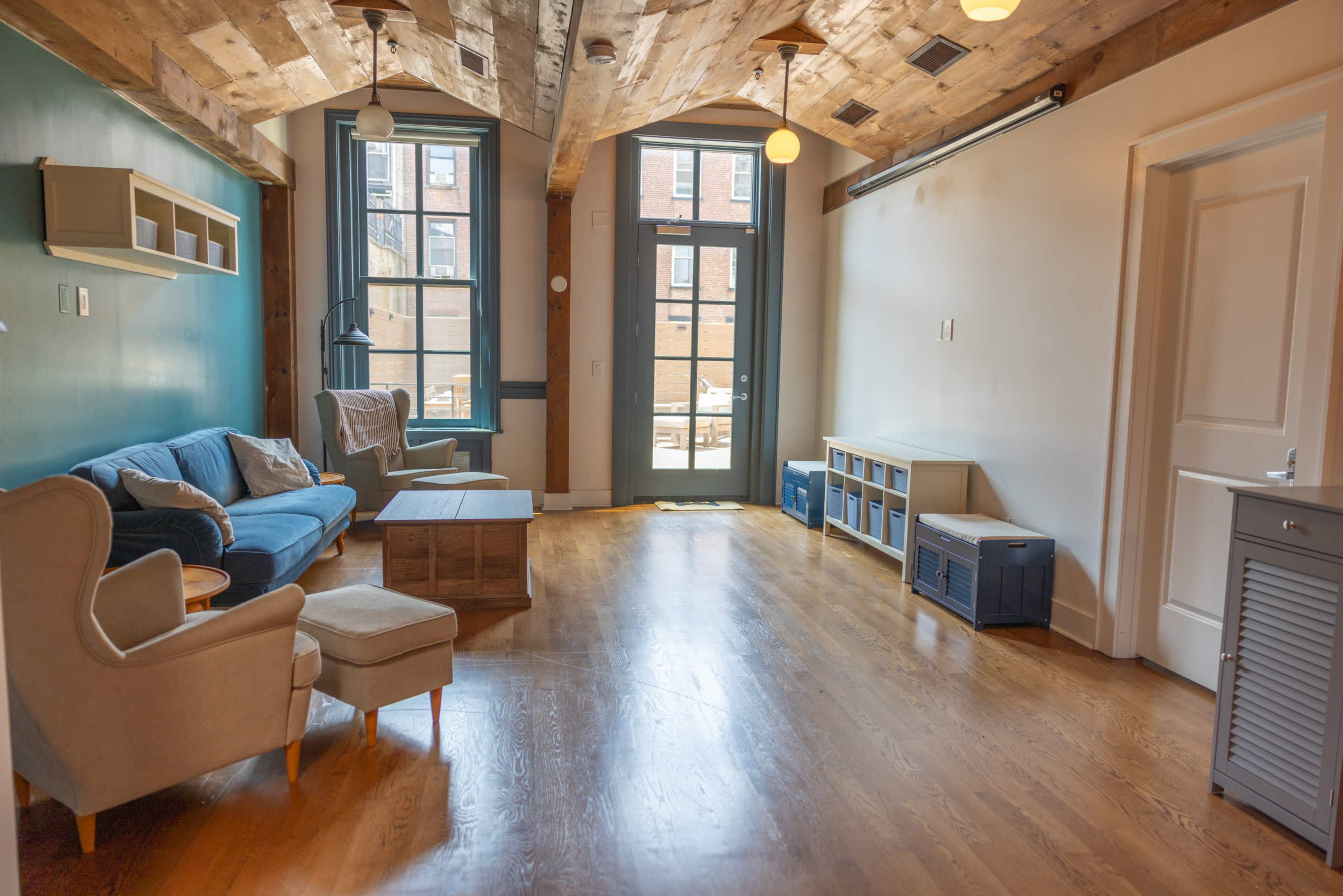 A spacious, well-lit living room with hardwood floors, featuring a blue sofa, a coffee table, and large windows that open to a patio area.