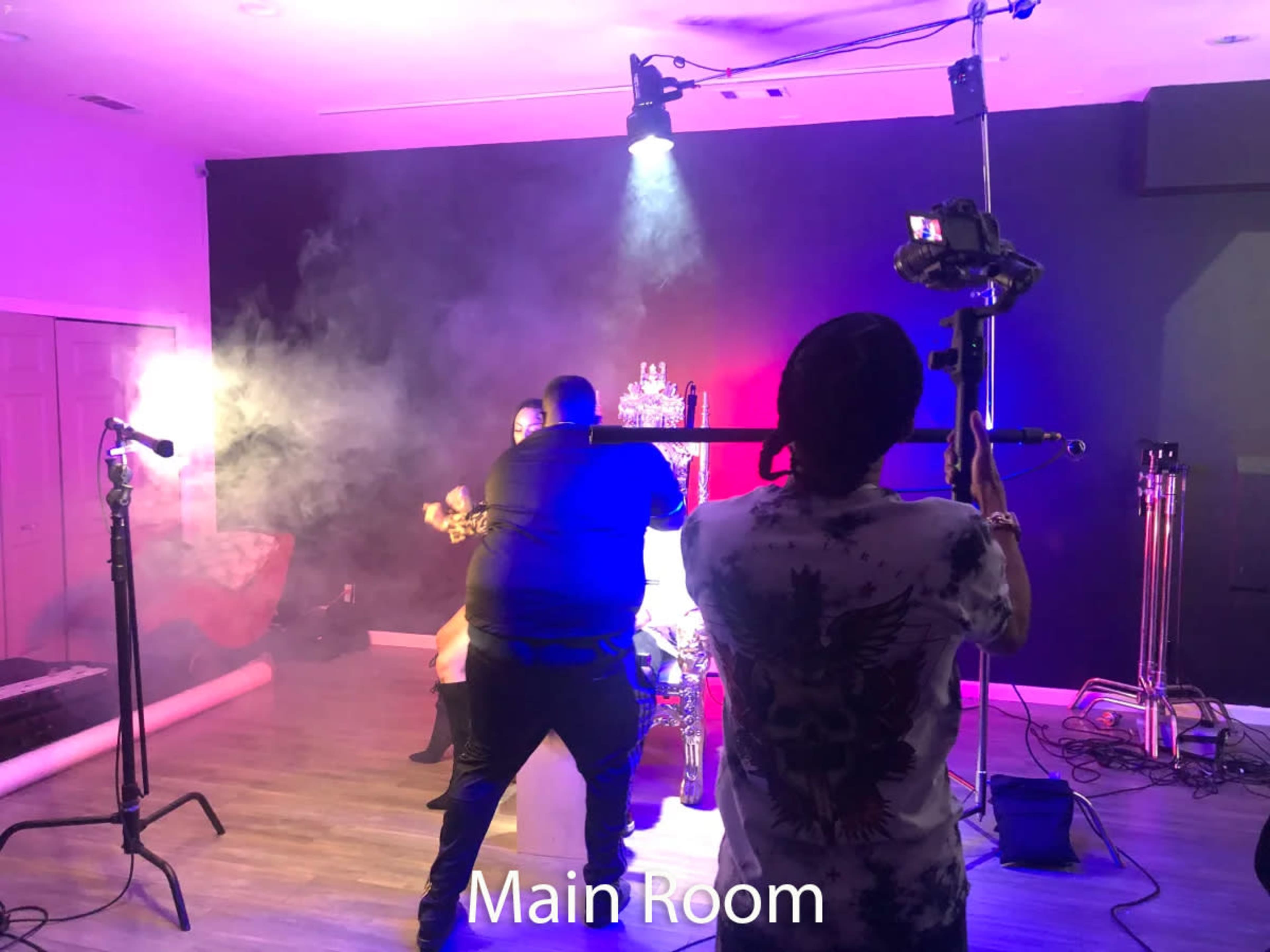 A person is filming a scene in a studio with smoke effects and various lighting setups while another person adjusts the shot.