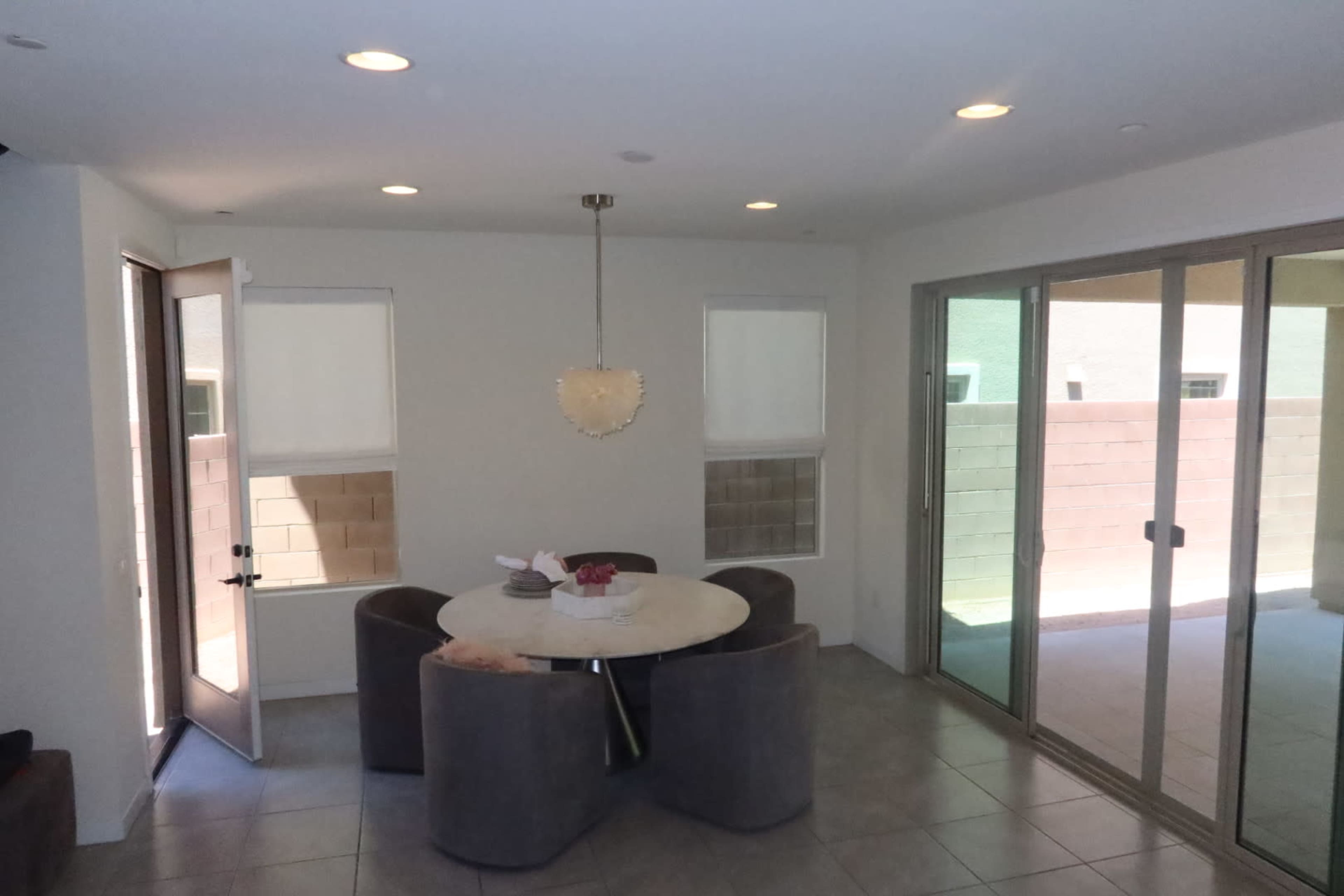 A circular table with gray chairs is centrally located in a brightly lit dining area, featuring large sliding glass doors that lead to an outdoor space.