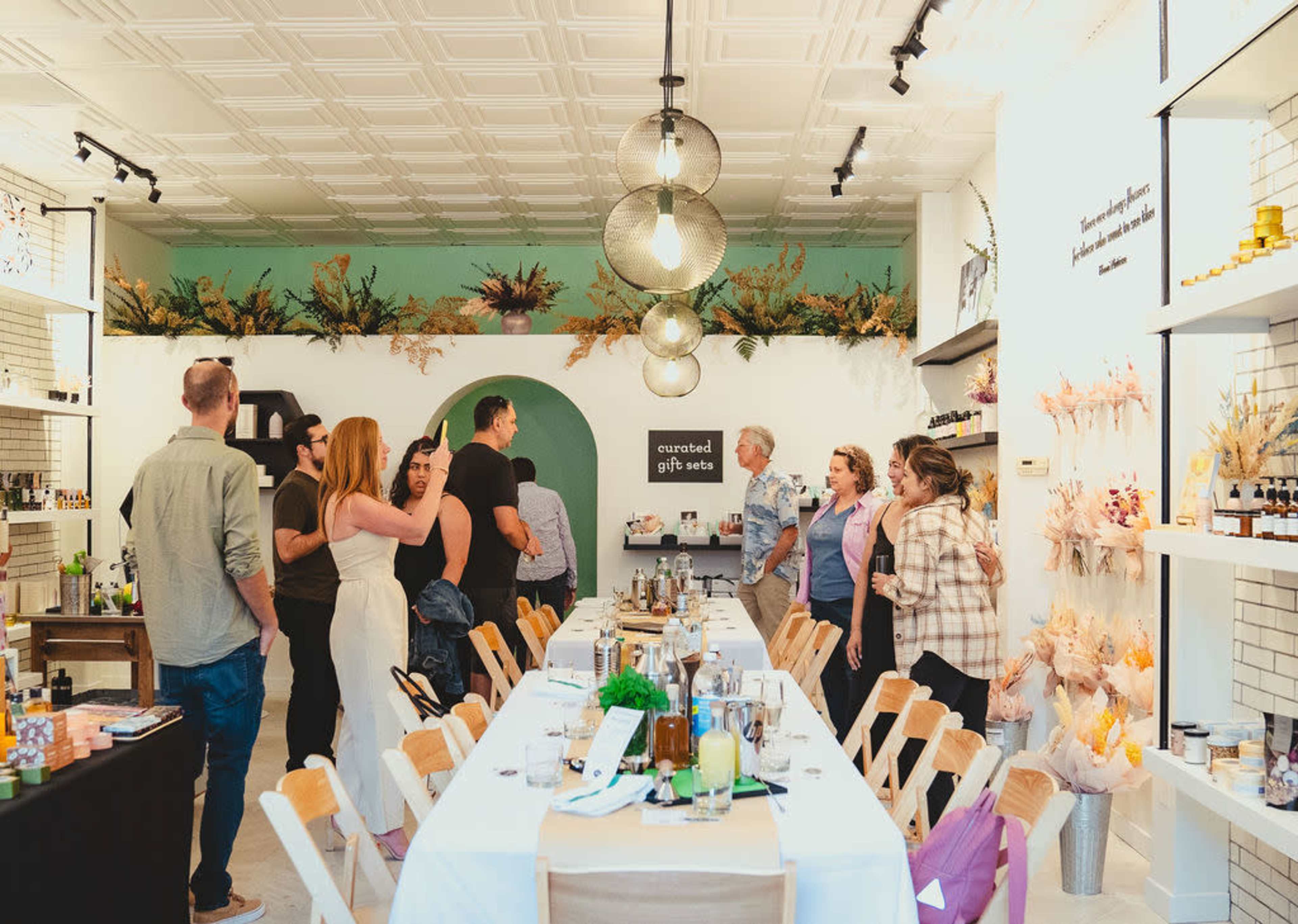 A group of people stands around a long table in a well-decorated shop filled with plants and gift items.