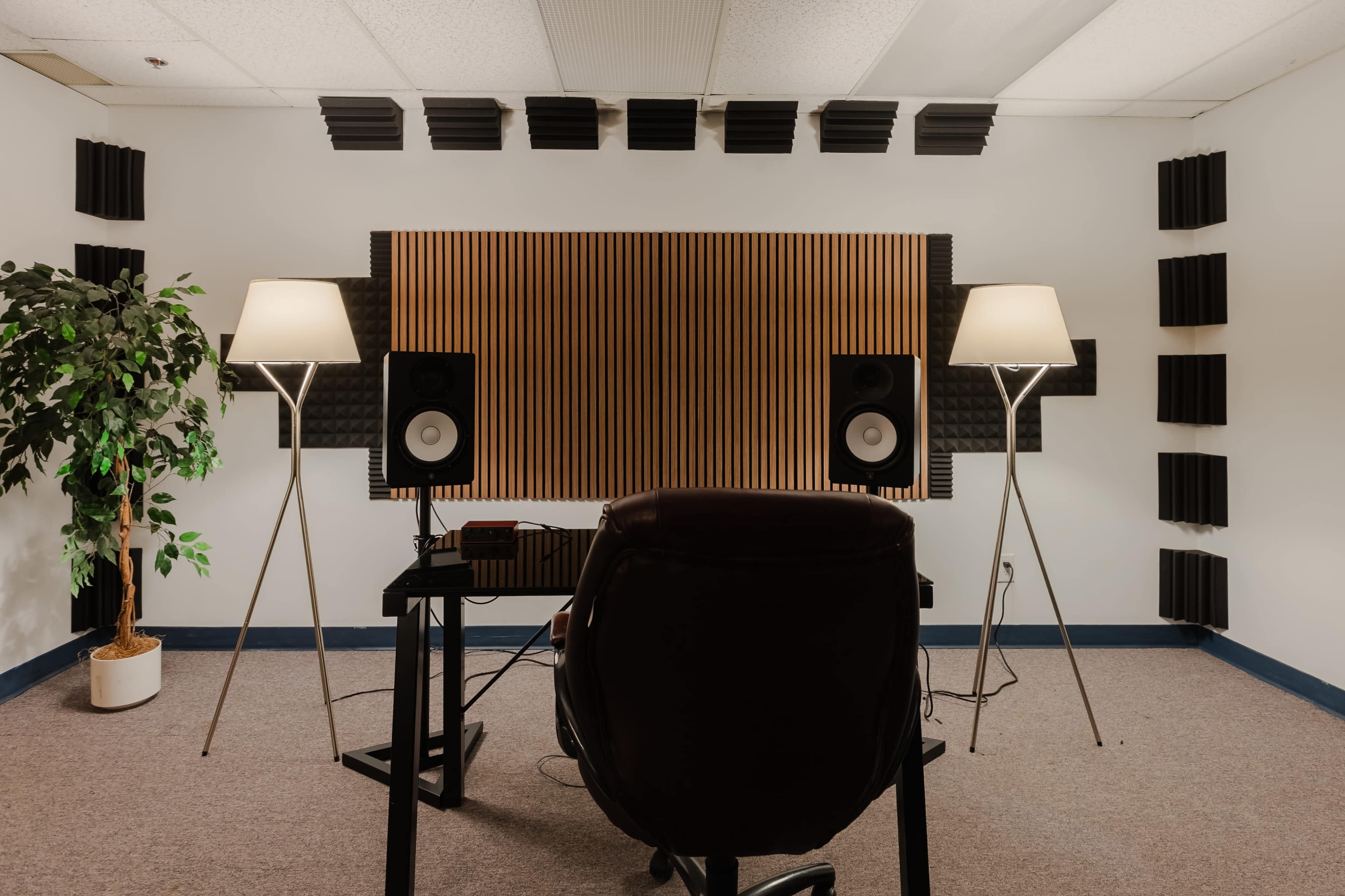 The image shows a soundproof studio featuring a desk with a chair, two audio speakers on either side, and acoustic panels on the walls.