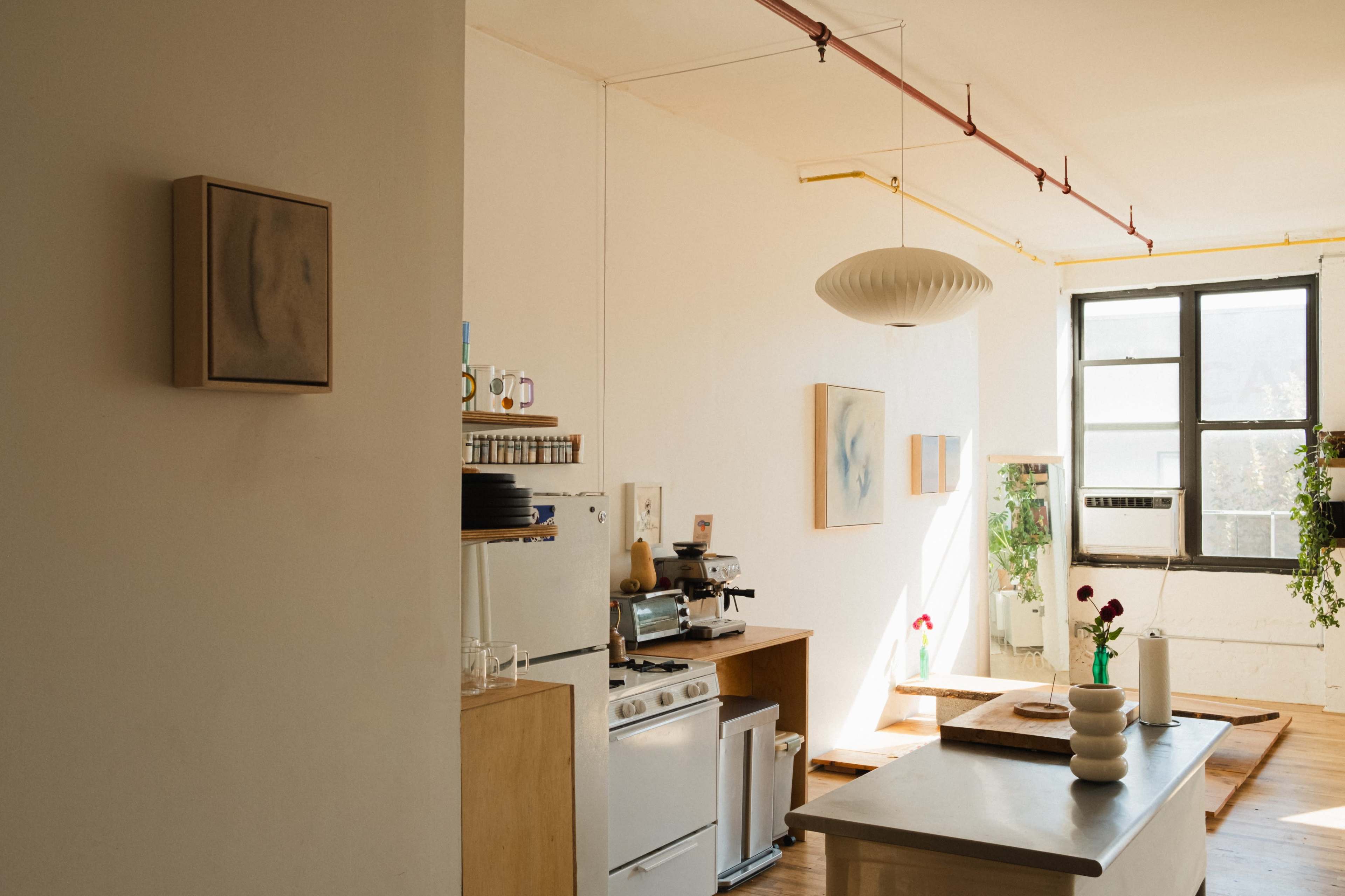 The image shows a bright, minimalist kitchen with wooden cabinets, a stove, and a large window.