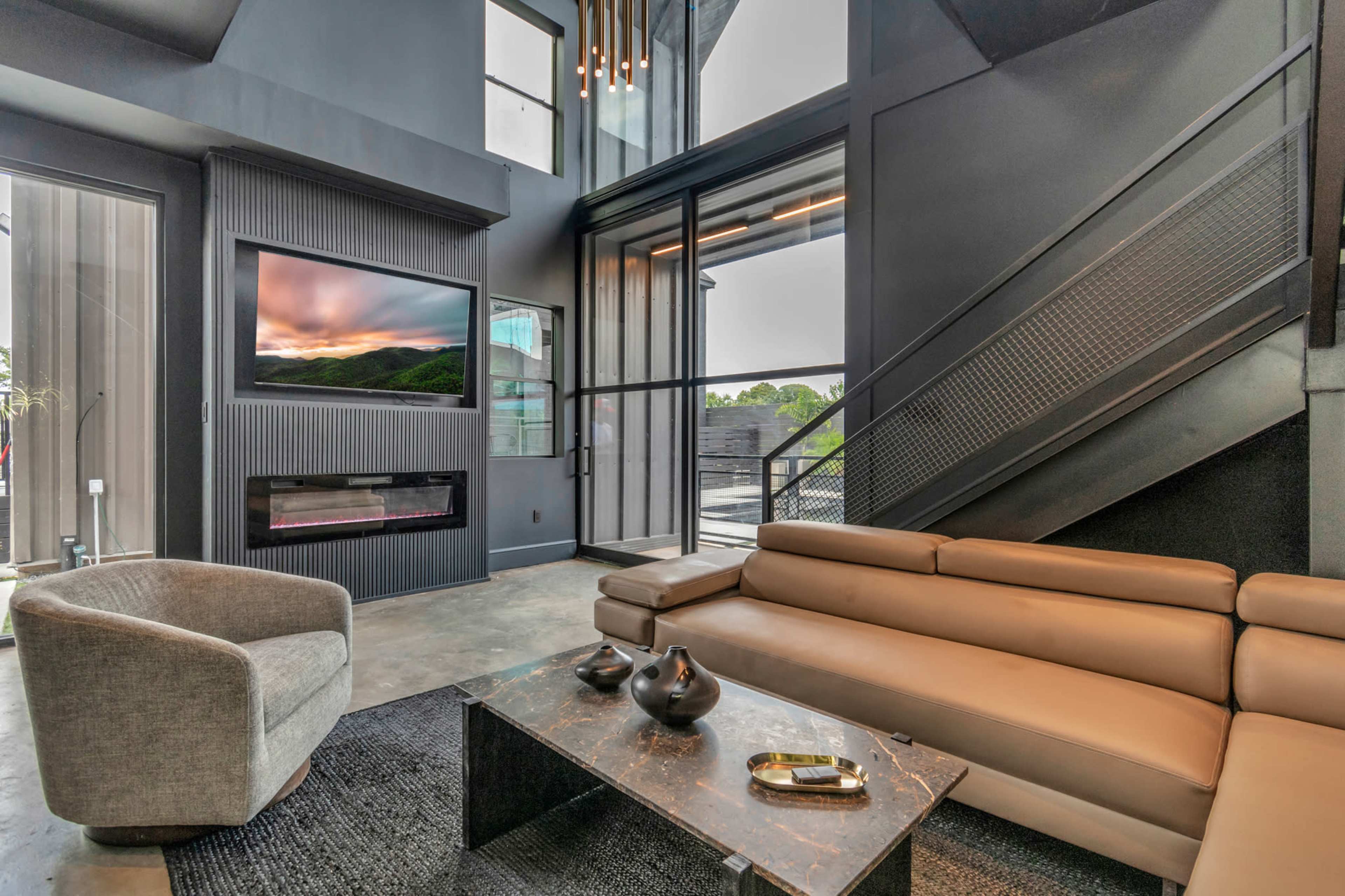 The image shows a modern living room with a sleek sectional sofa, a marble coffee table, and large windows showcasing an outdoor view.