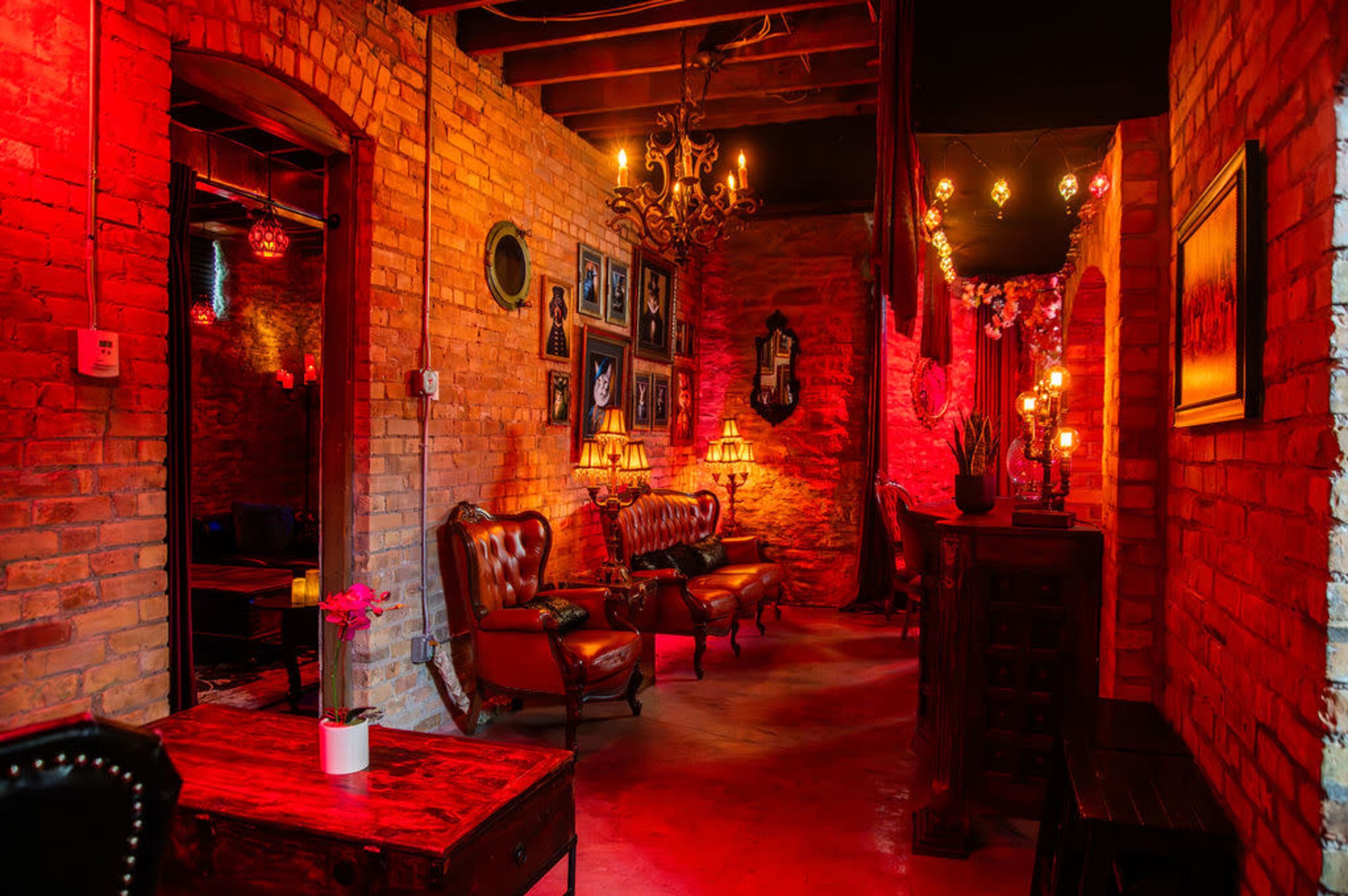 The image shows a dimly lit corridor in a brick-walled room featuring vintage furniture, chandeliers, and decorative wall art.
