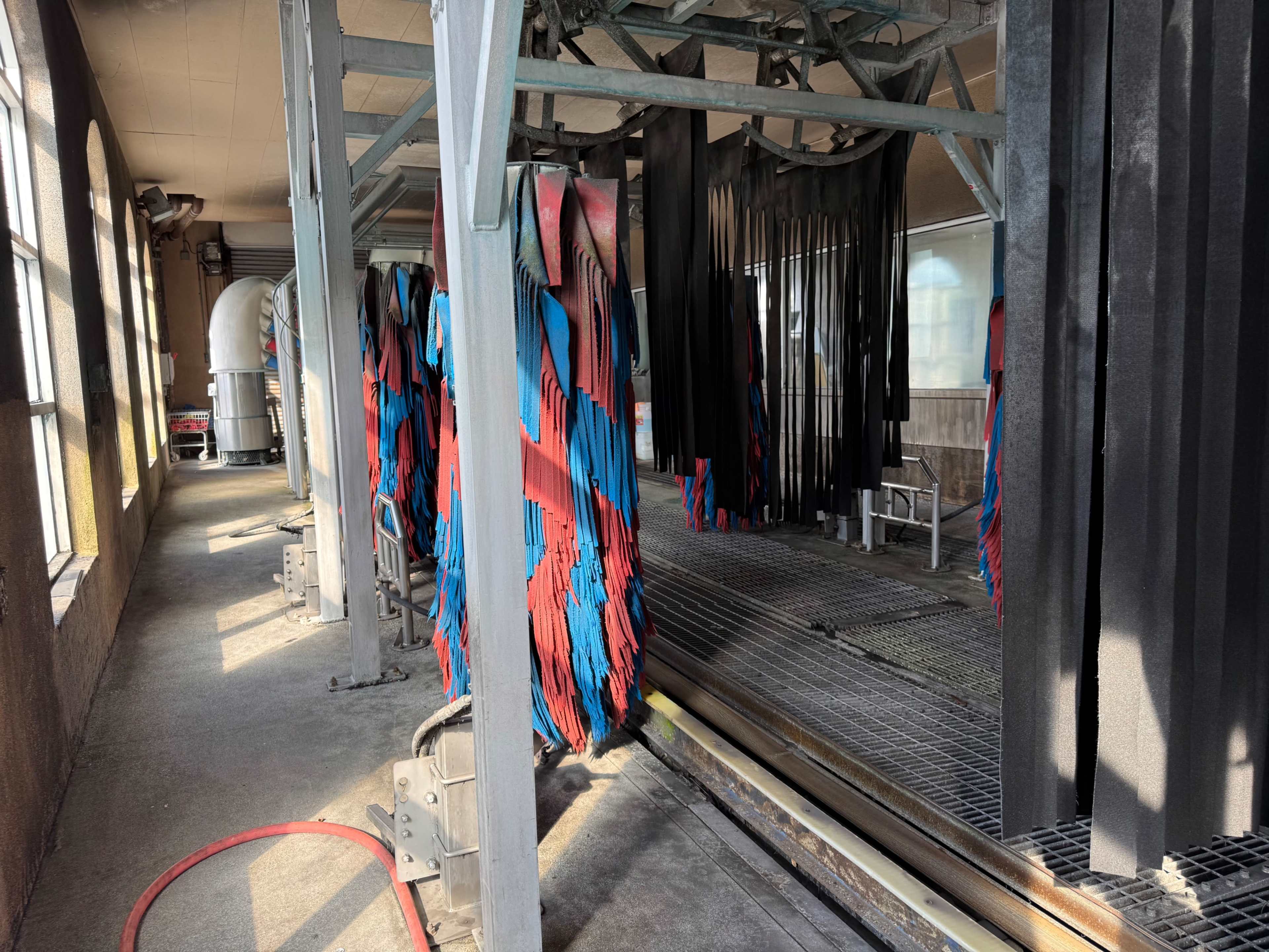 The image shows a car wash facility with hanging strips of cleaning material and a concrete floor.