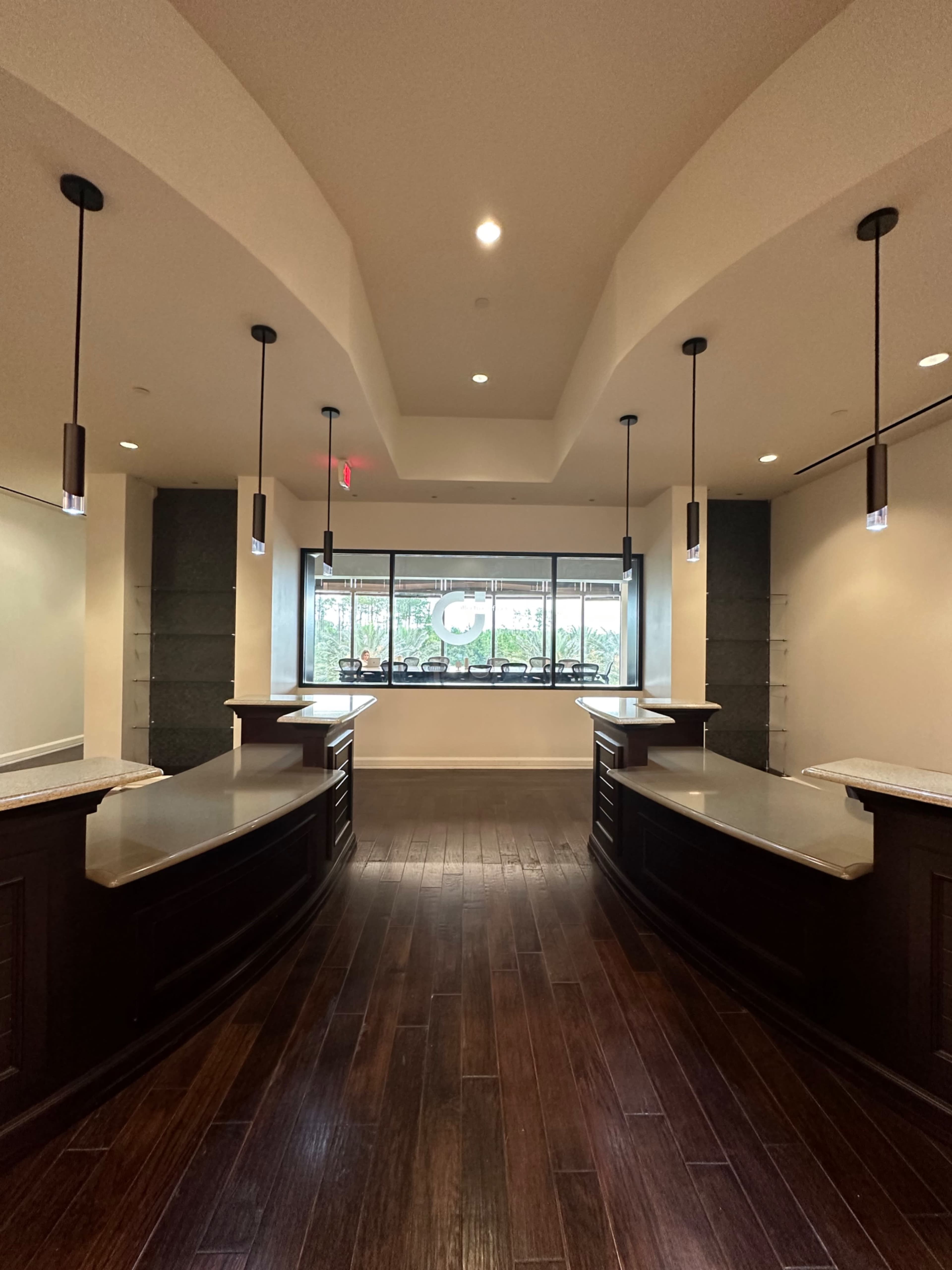 A spacious interior with two dark wooden reception desks facing a large window that overlooks a garden.