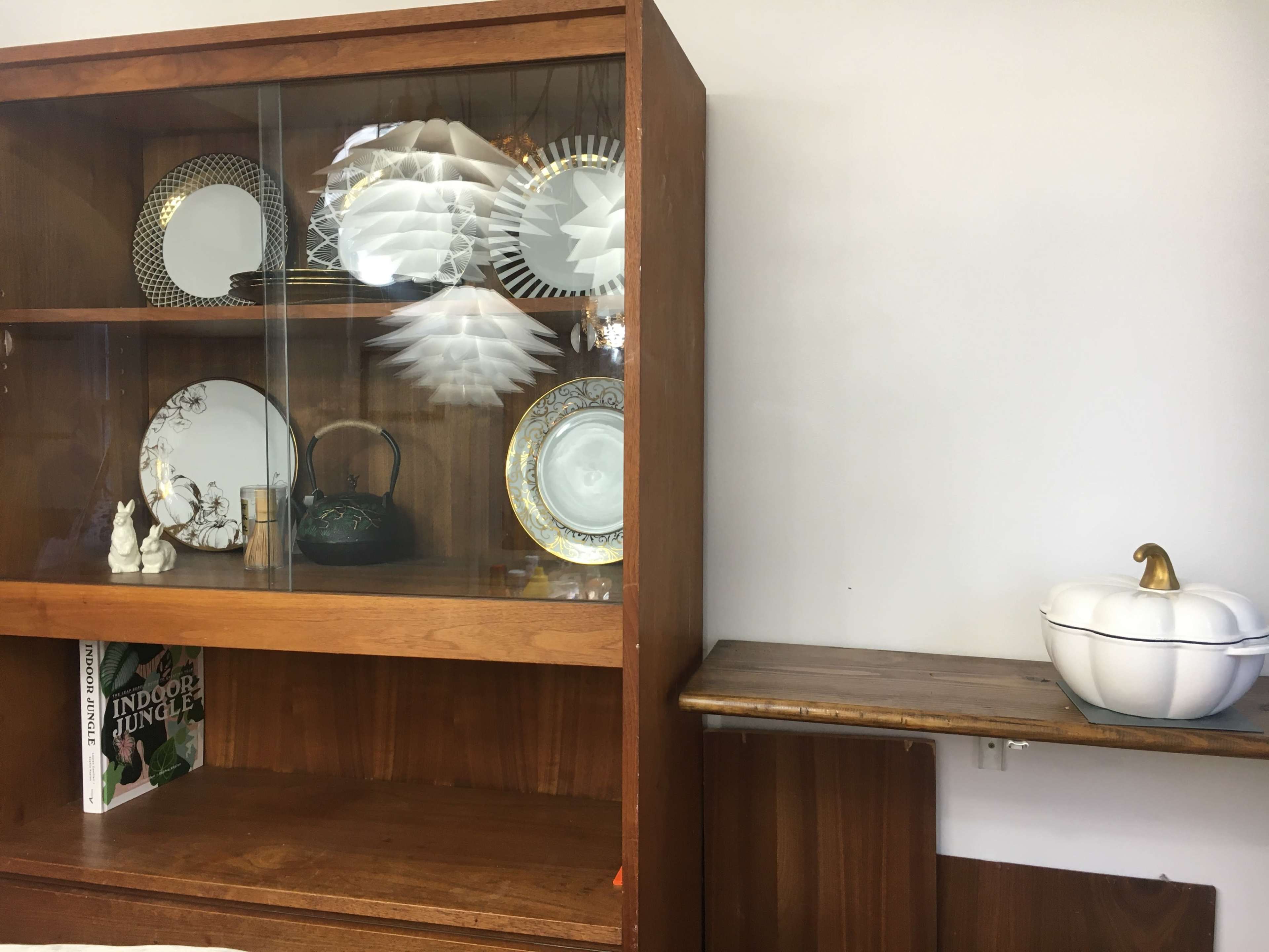 A wooden display cabinet holds various decorative plates and items, while a small white bowl rests on a nearby wooden shelf.