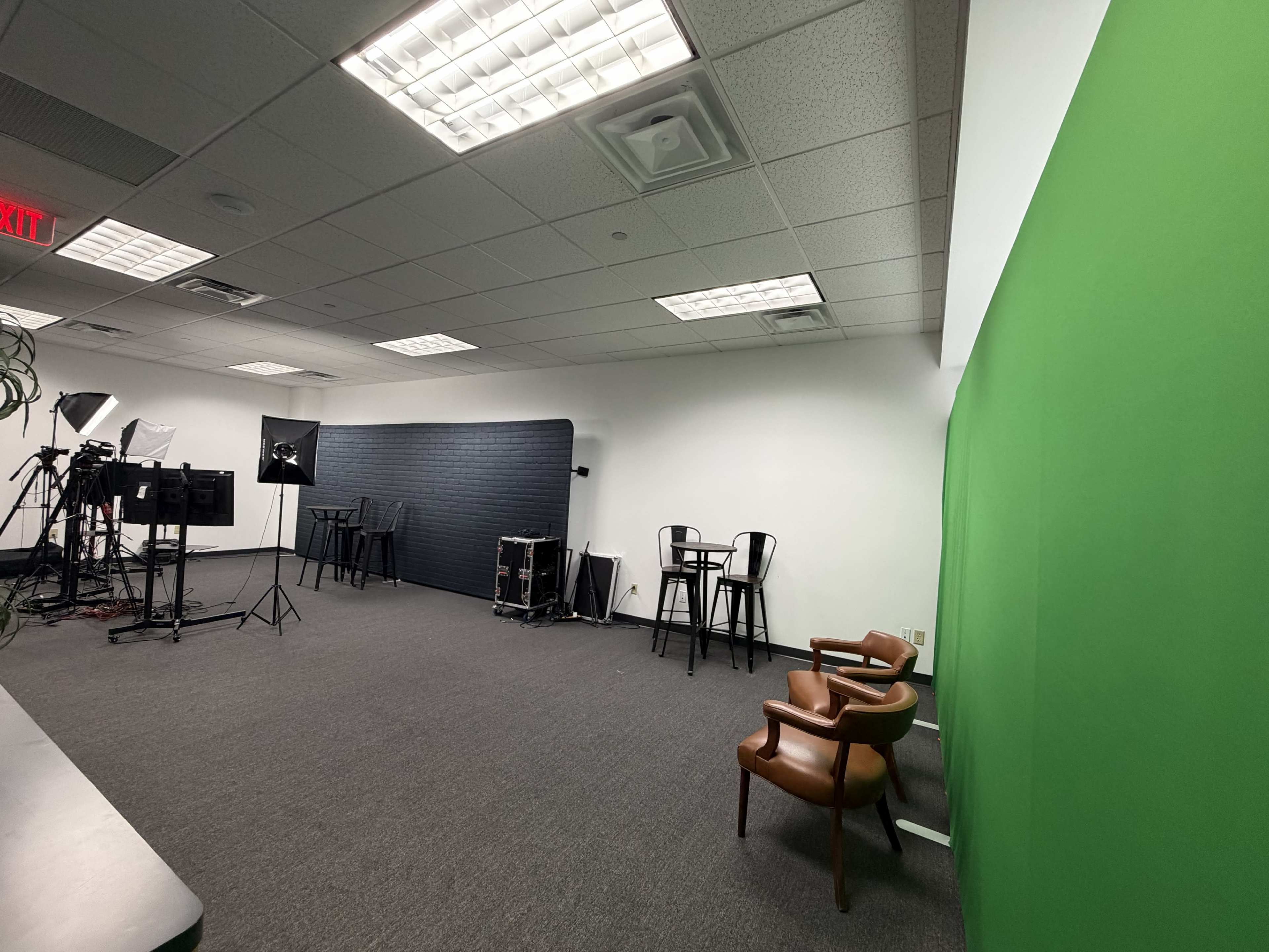 The image shows a minimalist studio space with a green screen, two chairs, and several lighting equipment setups against a gray backdrop.