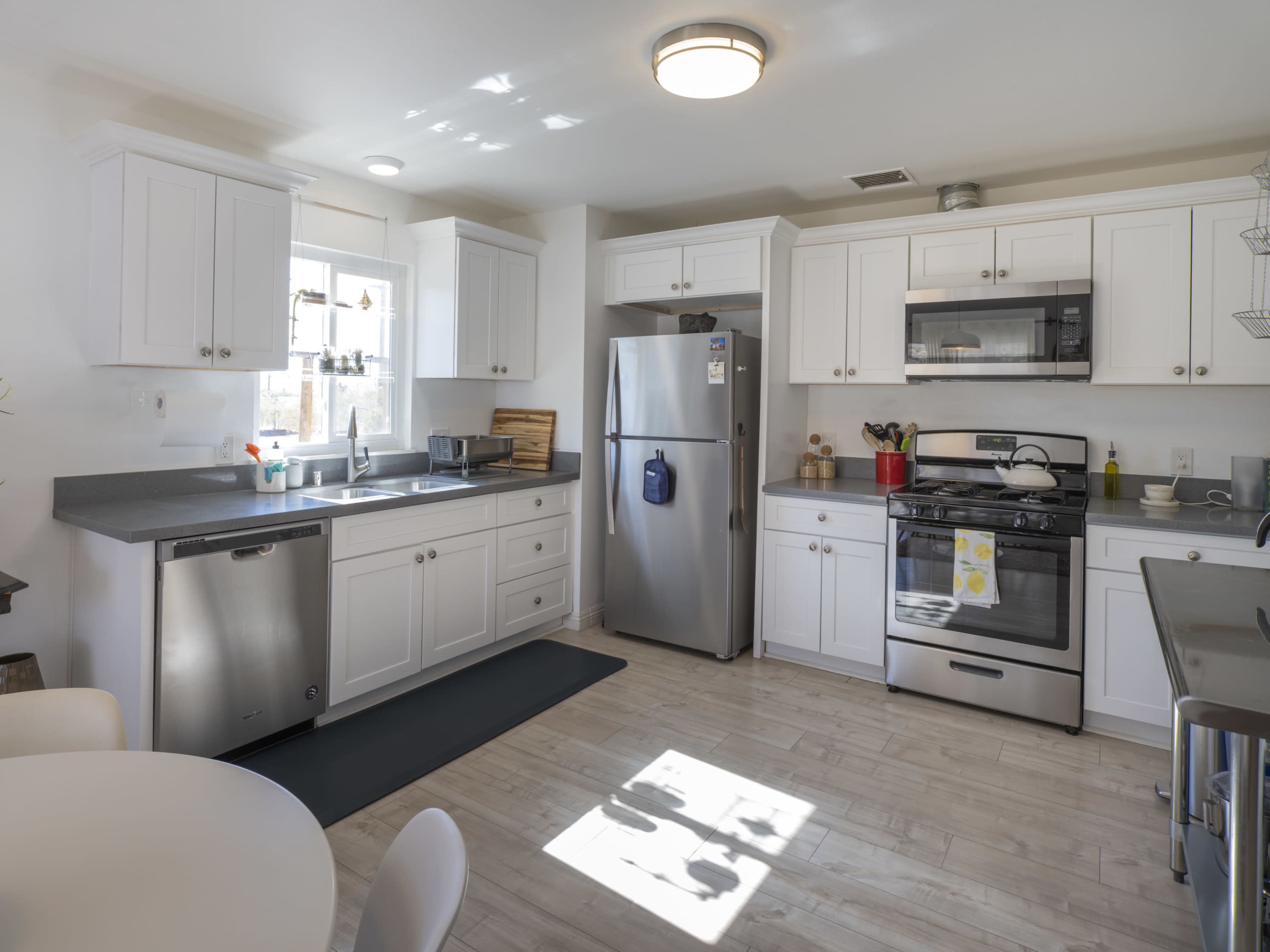 A modern kitchen features white cabinets, stainless steel appliances, and a gray countertop with a small dining table in the corner.