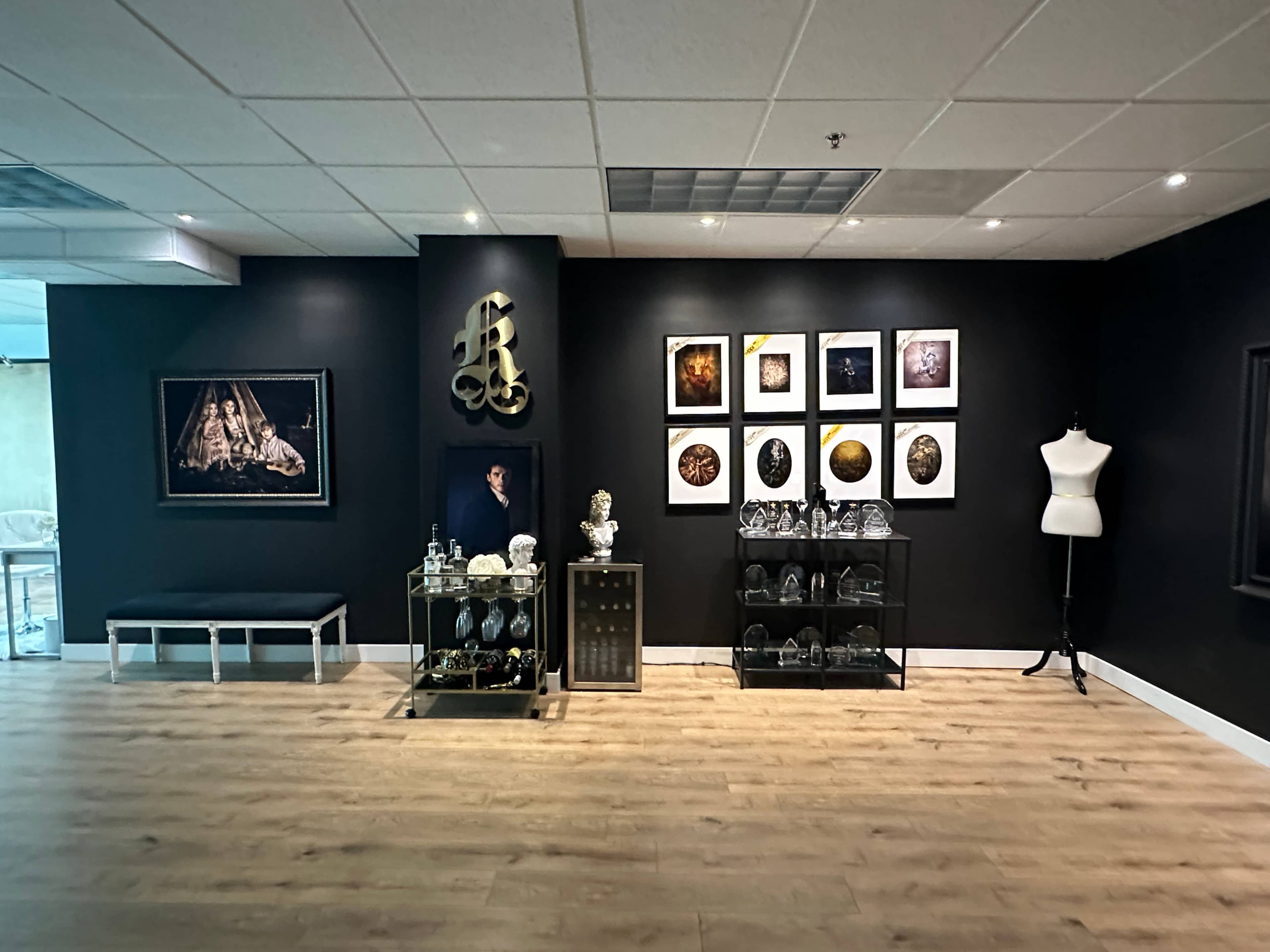 The image shows an art gallery with a dark wall displaying framed artworks, a glass display case filled with decorative items, and a mannequin standing in the corner.