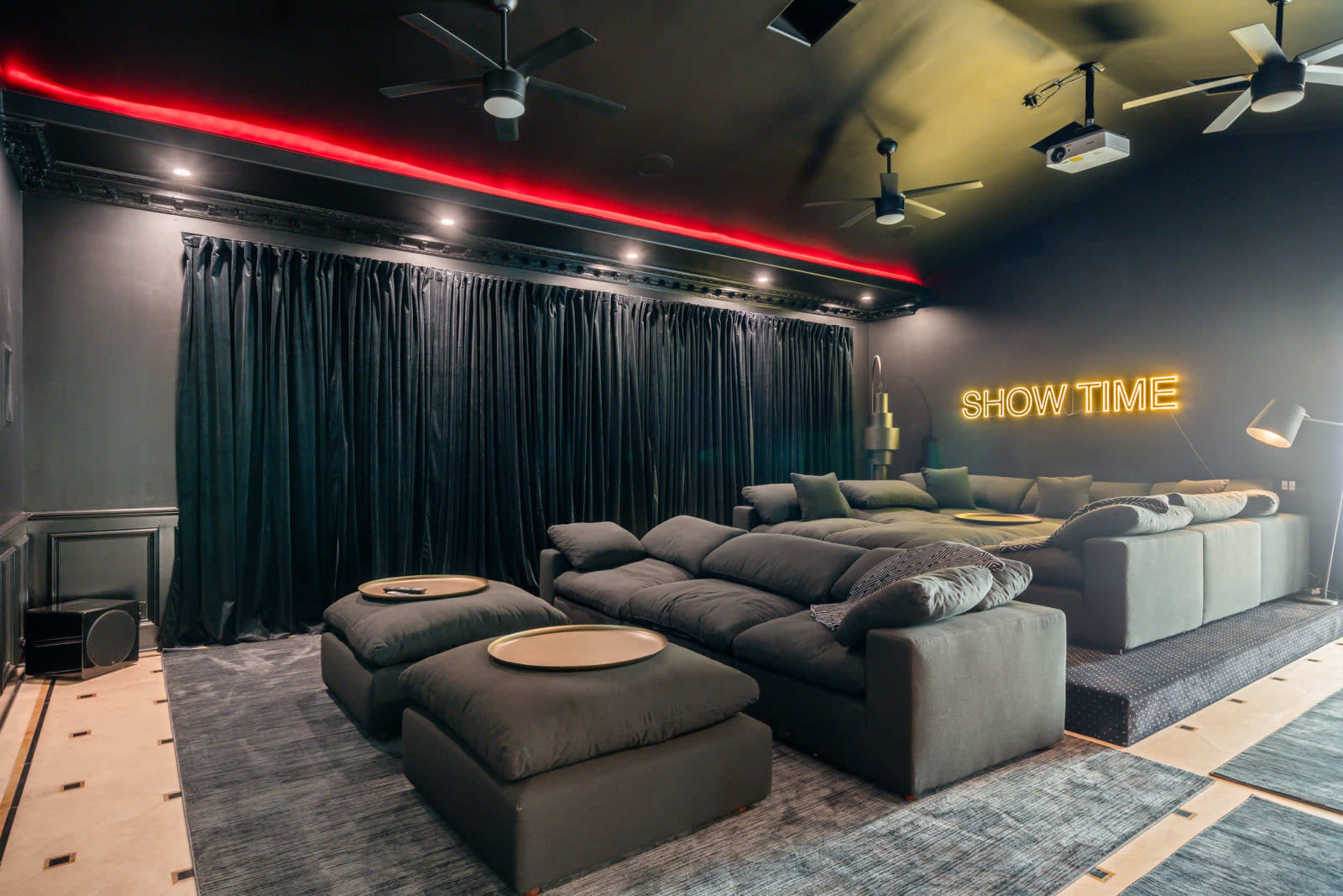 A home theater room with black walls, plush seating, and a neon sign that reads "SHOW TIME."