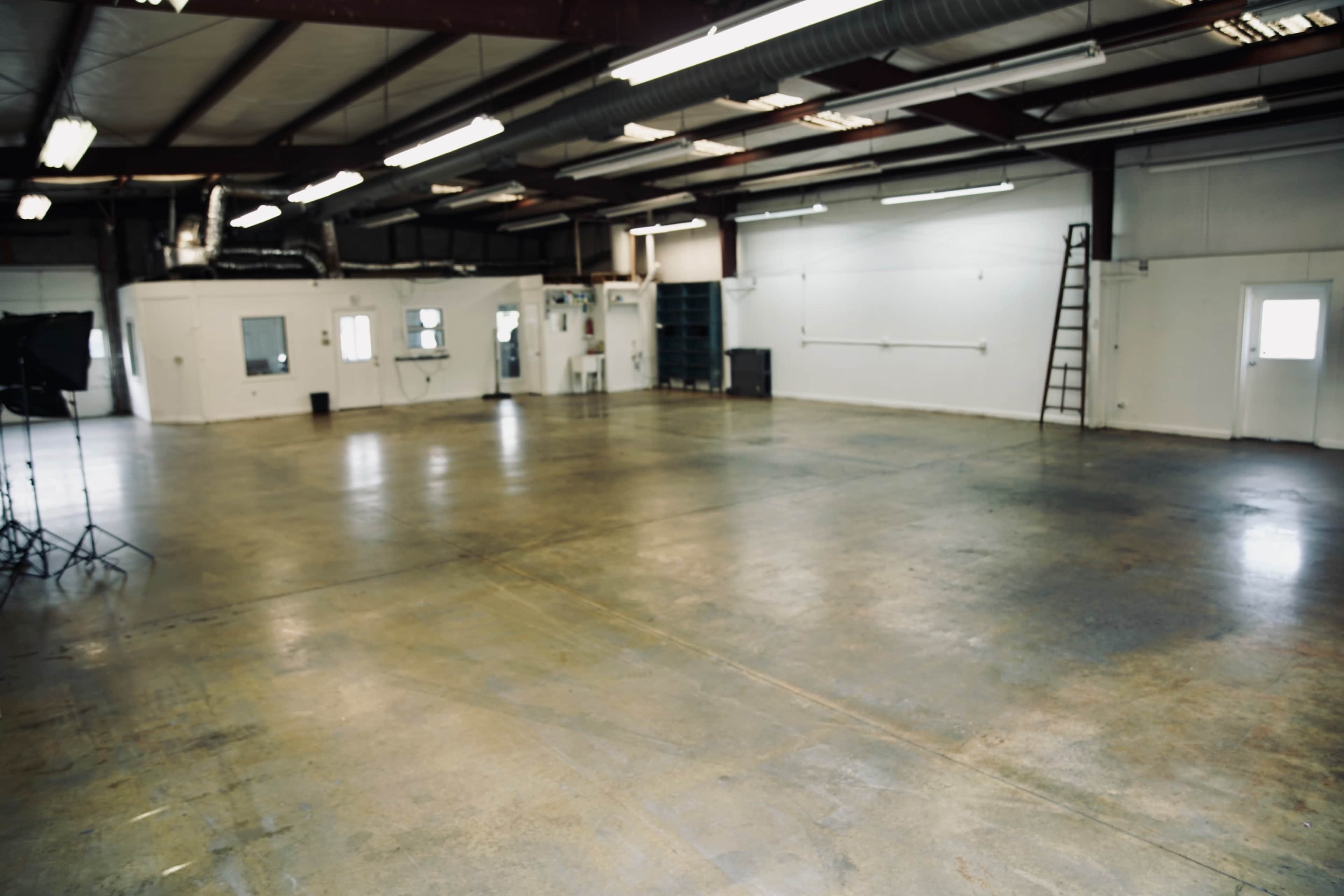 The image shows an empty industrial space with a concrete floor, overhead lights, and a ladder against the wall.